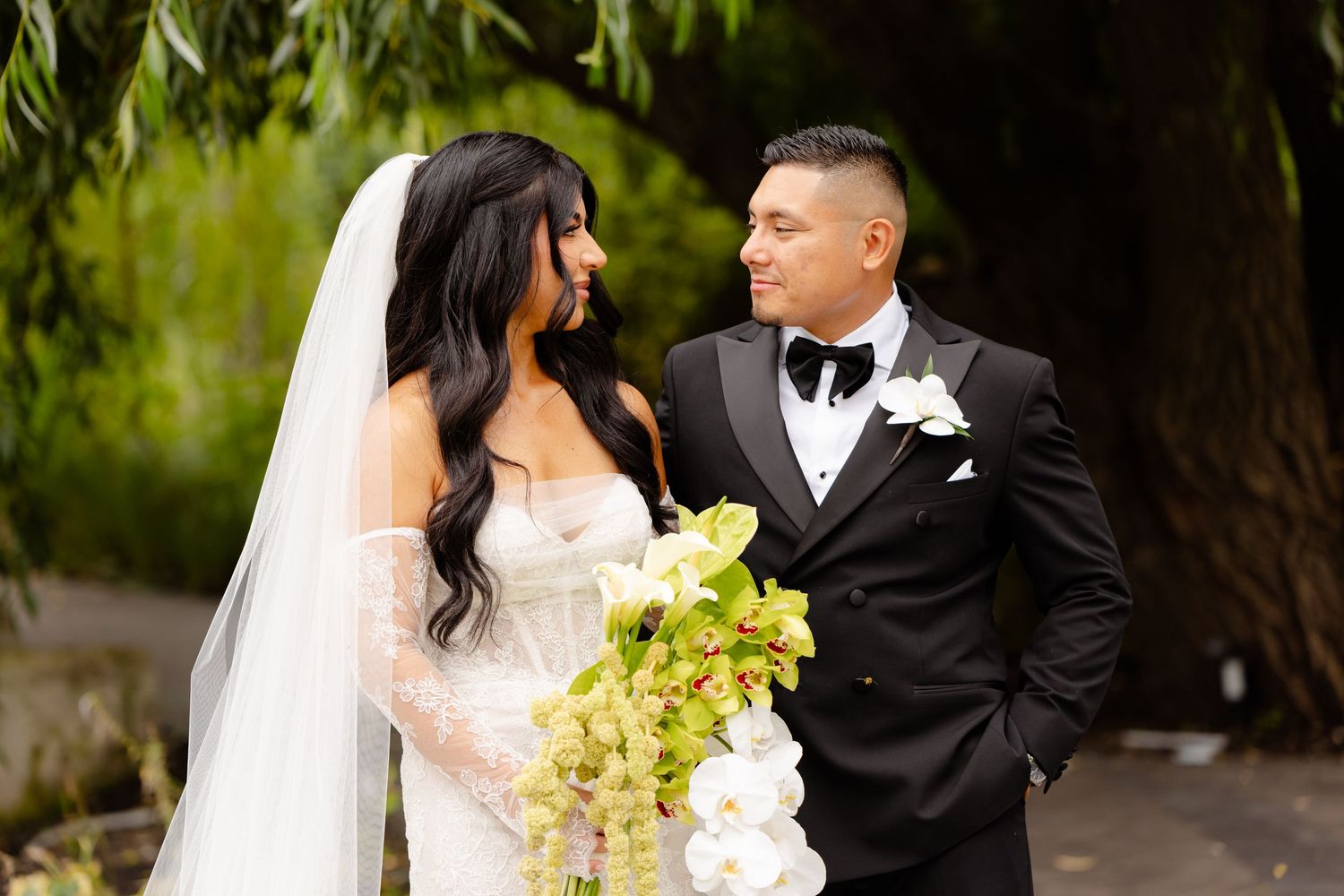Bride and groom share intimate moments in a garden setting while holding a bouquet of yellow orchids.