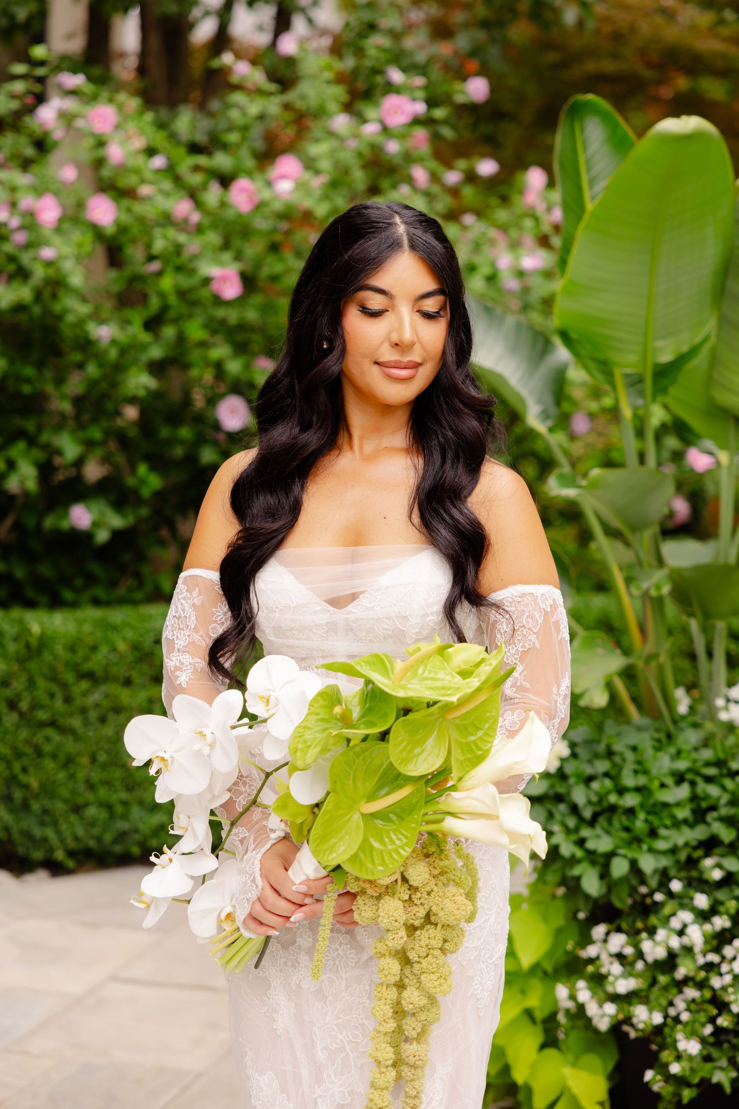 A detailed wedding photography shot in a lush garden setting with pink flowers and greenery.