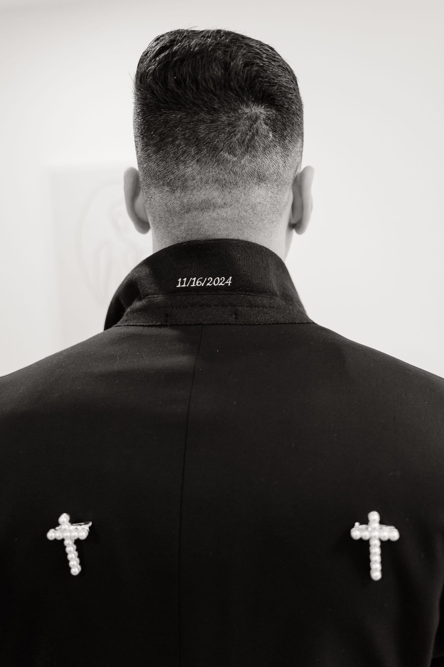 Back view of a formal black suit jacket with embroidered crosses and date detail.