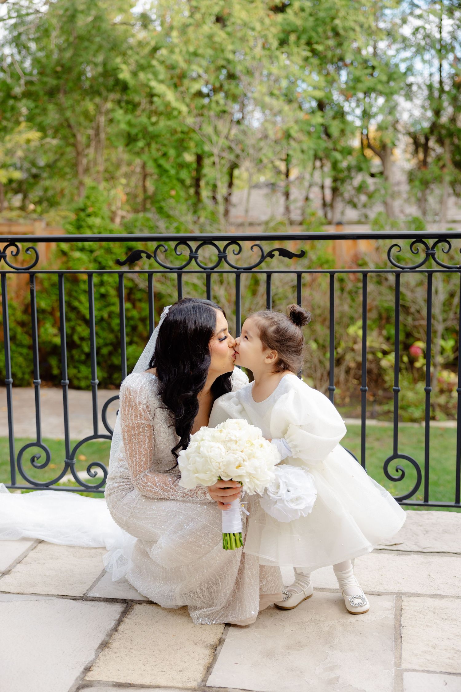 Sweet moment captured between bride and flower girl sharing affectionate pose on outdoor balcony.