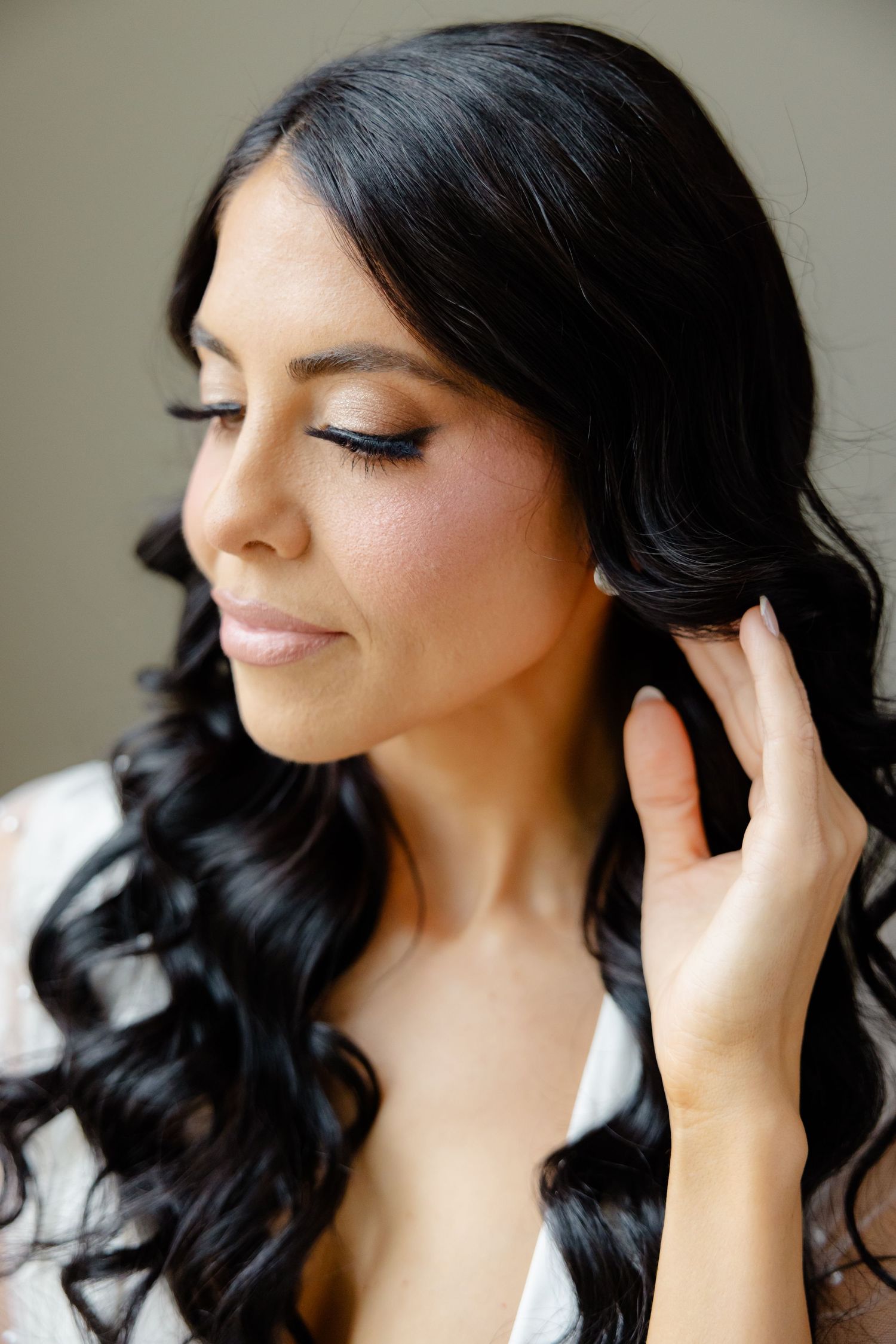 Close-up beauty shot showing styled dark waves and natural bridal makeup.