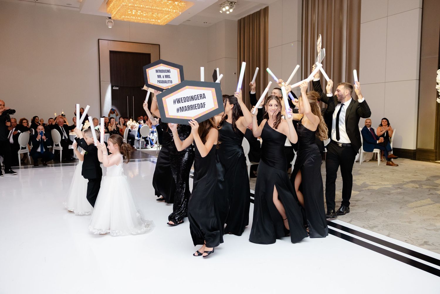 Dancers in formal black dresses and suits perform a choreographed line dance at an elegant ballroom event.