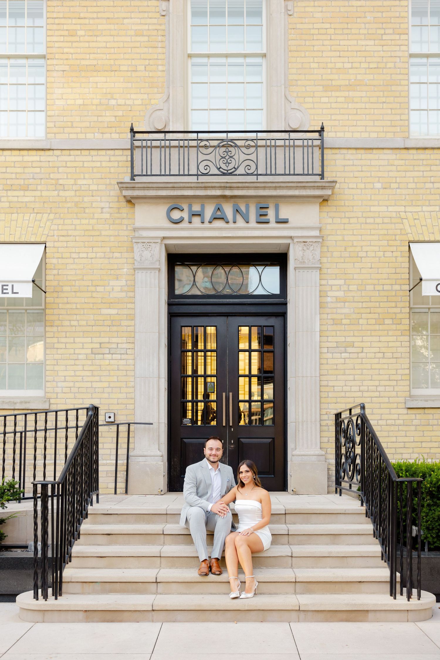 Couple seated on grand entrance steps of Chanel store with classic architectural details.