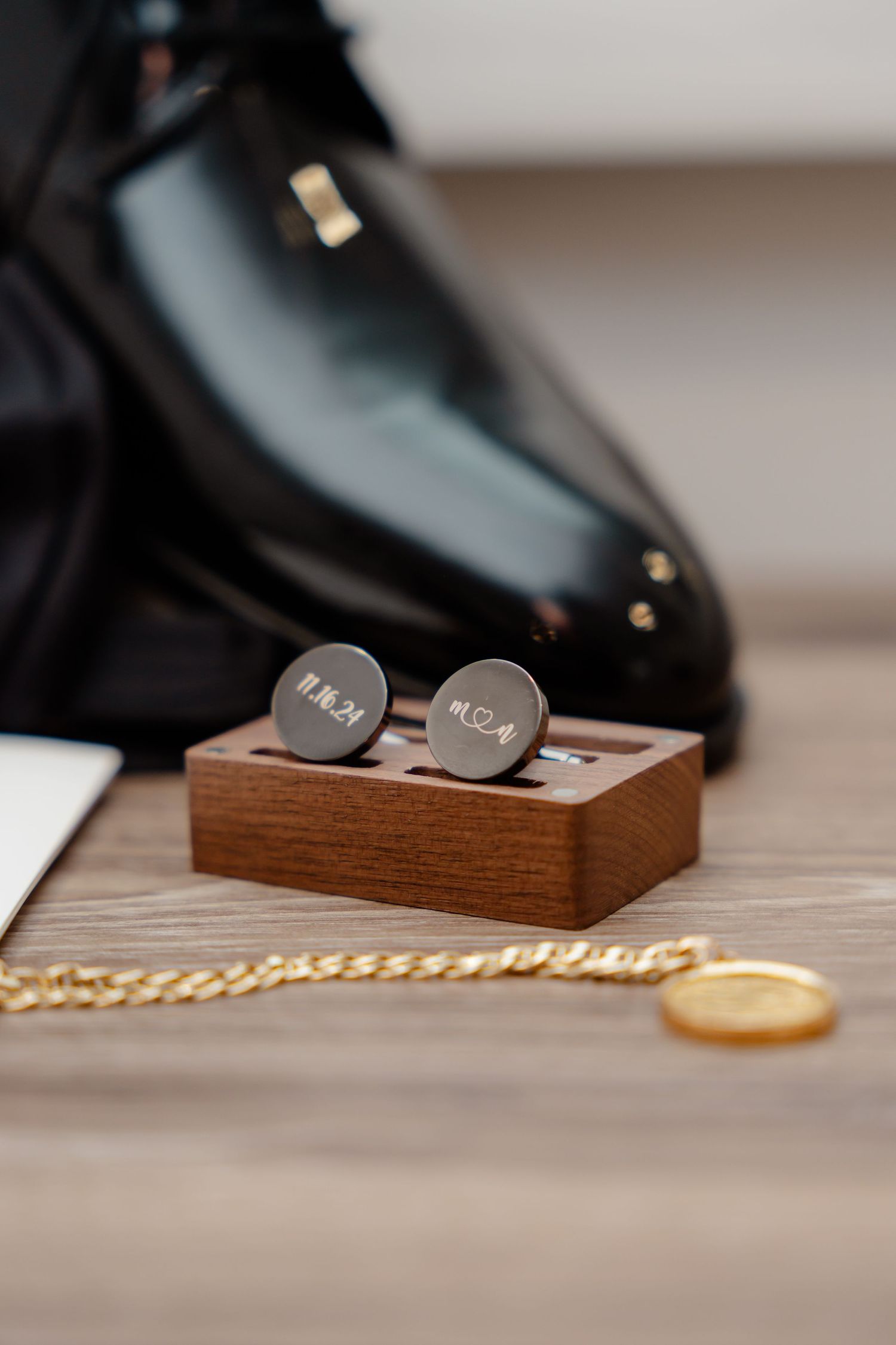 Engraved cufflinks in wooden box with dress shoes and gold chain.