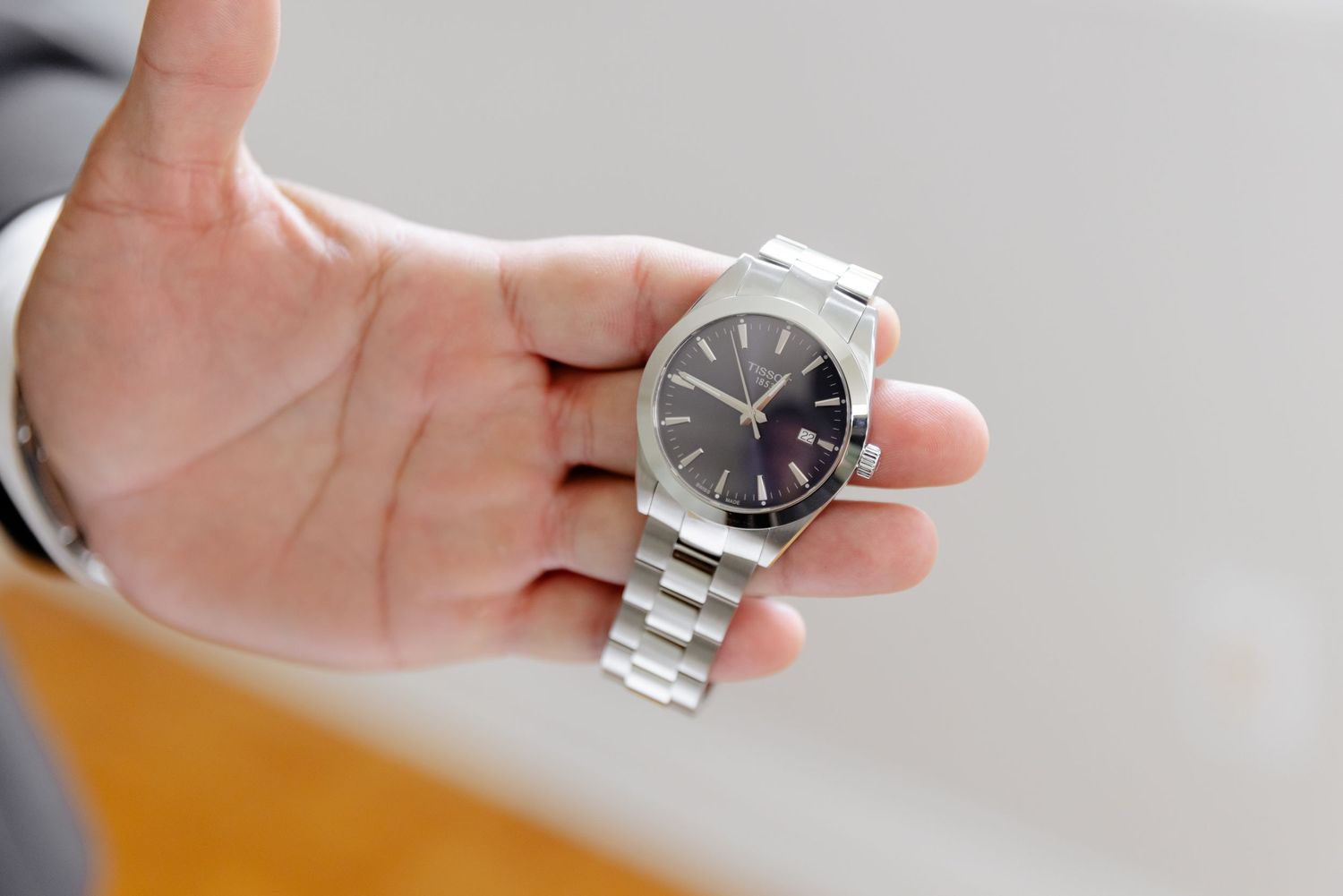 A silver wristwatch with analog display being adjusted by hands against a light background.