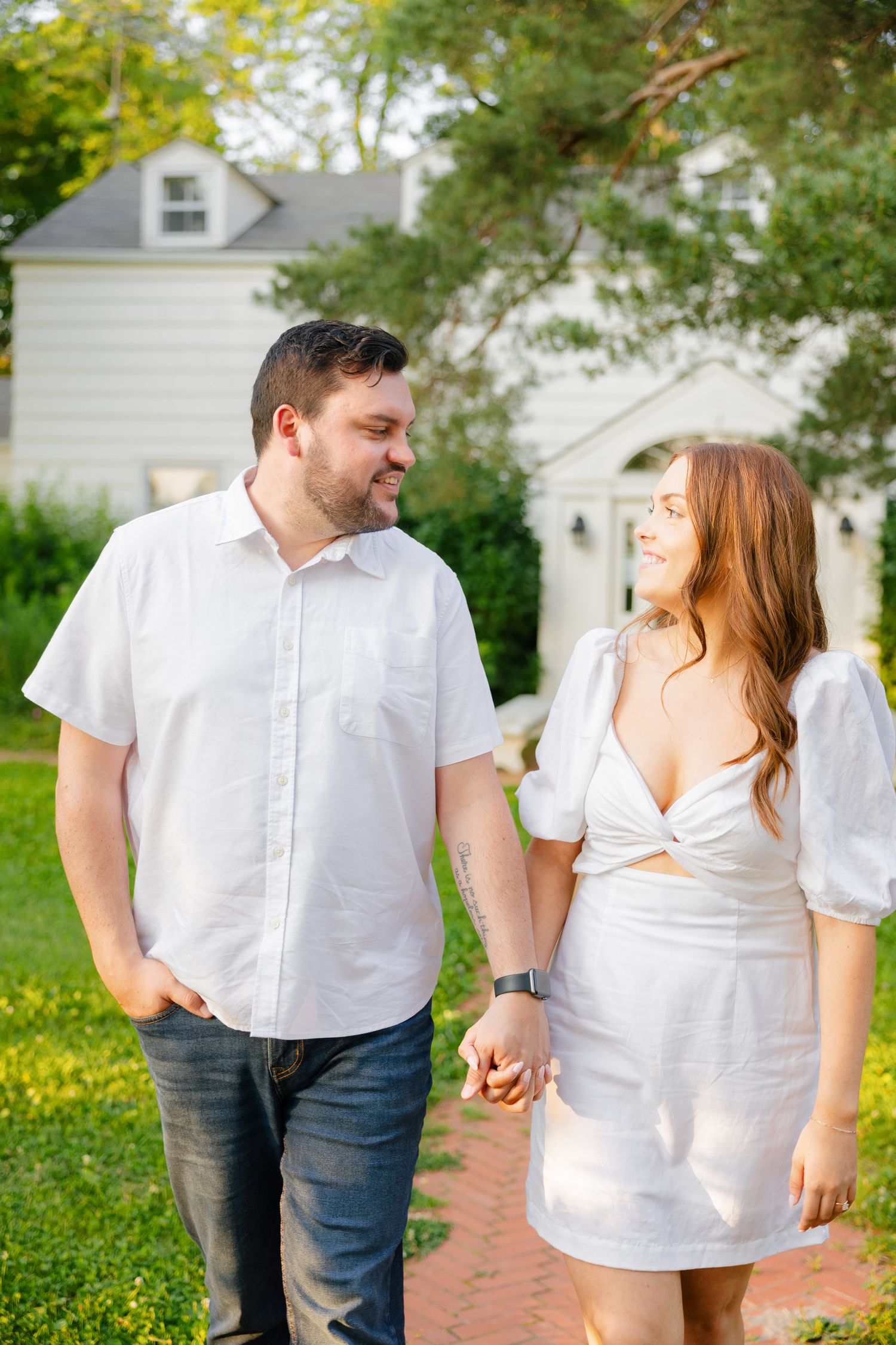 A couple in coordinating white outfits shares a casual moment on a brick pathway.