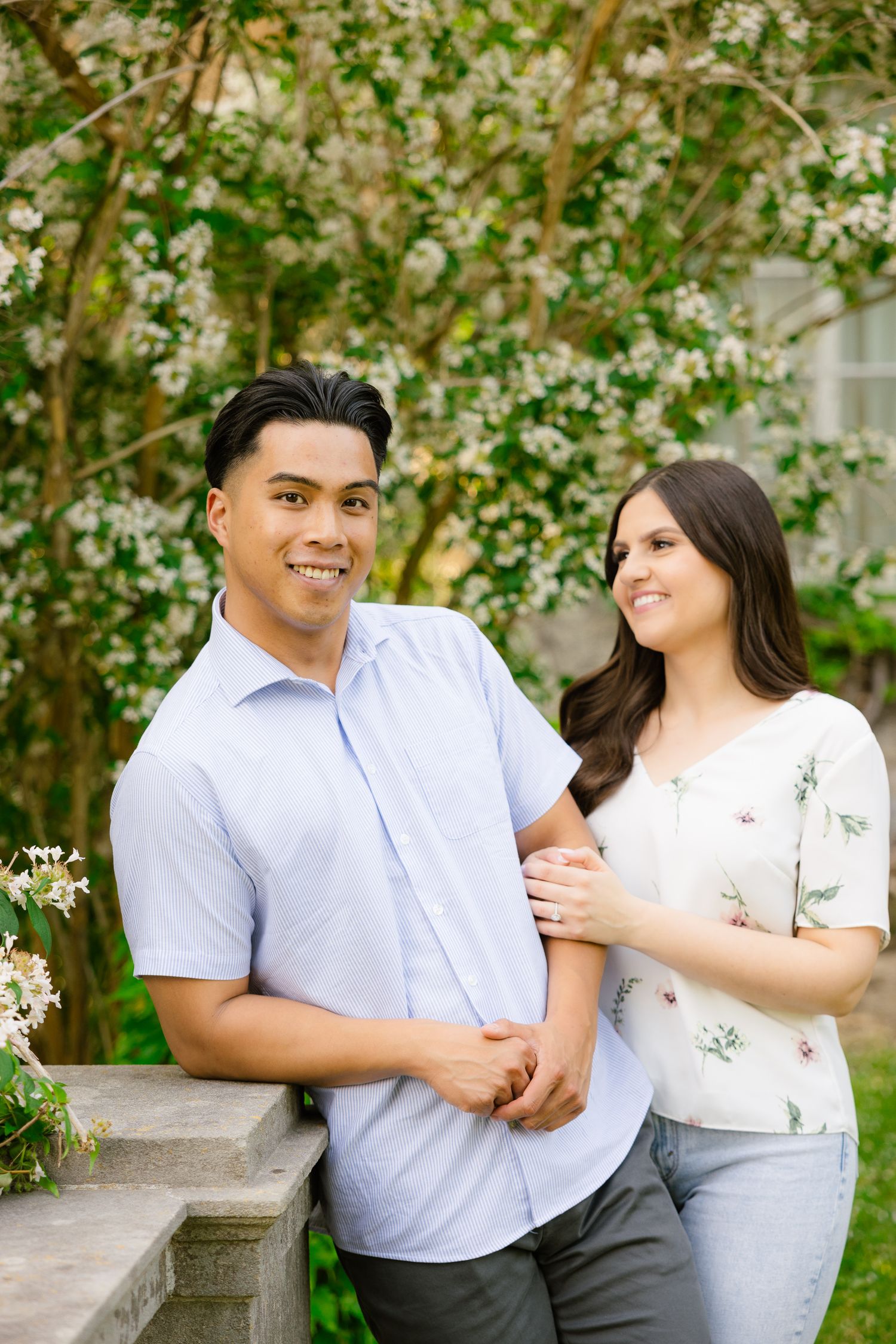 Happy couple stands by stone balustrade surrounded by spring blossoms.