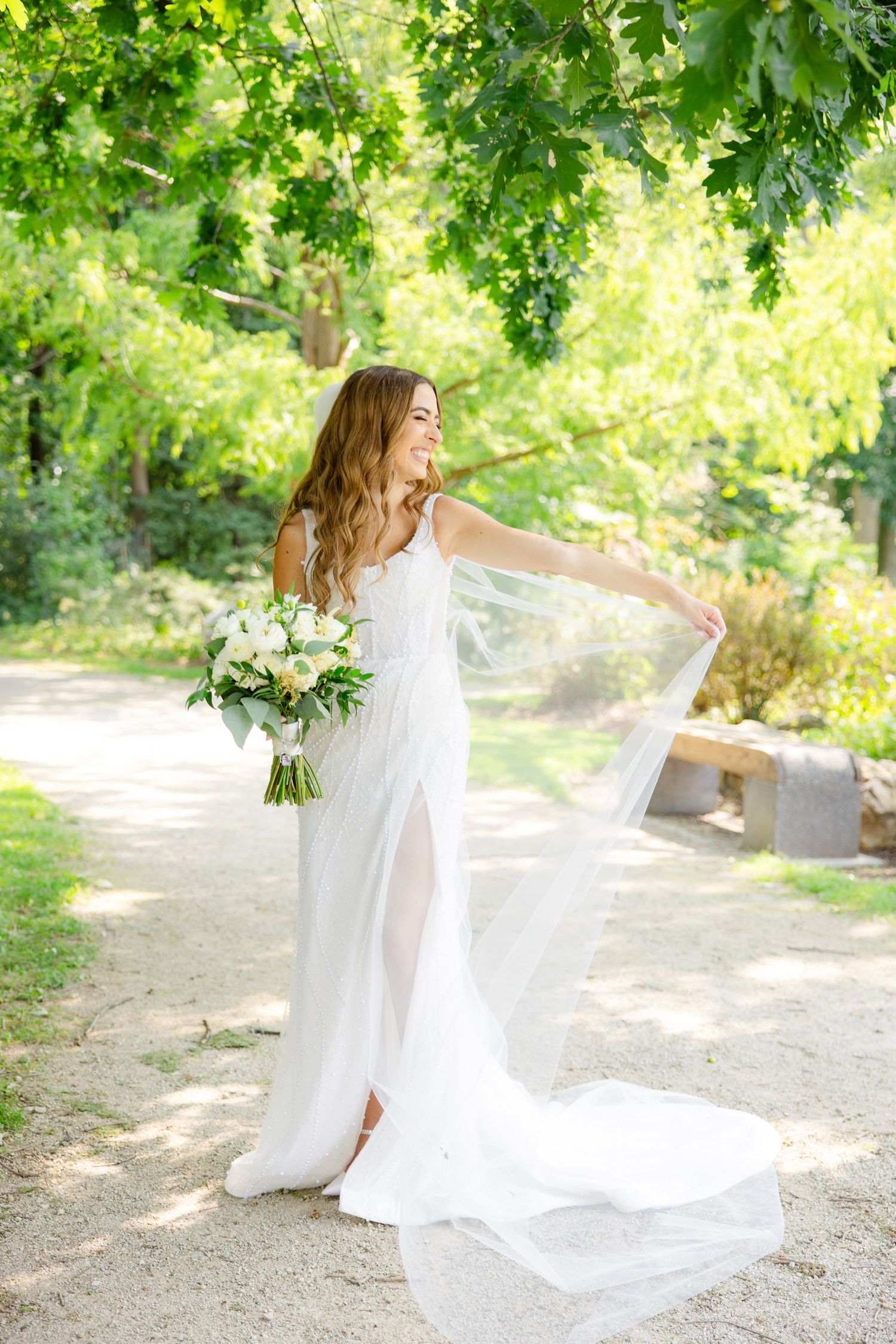 A flowing white wedding dress catches the breeze as bride holds bouquet in garden setting.