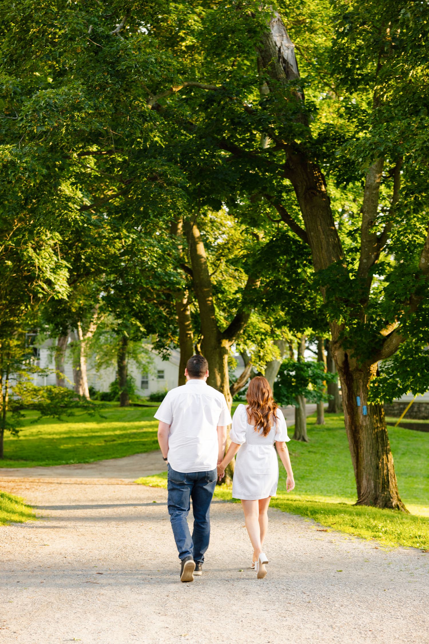 A couple strolls together on a peaceful path under a canopy of green trees.