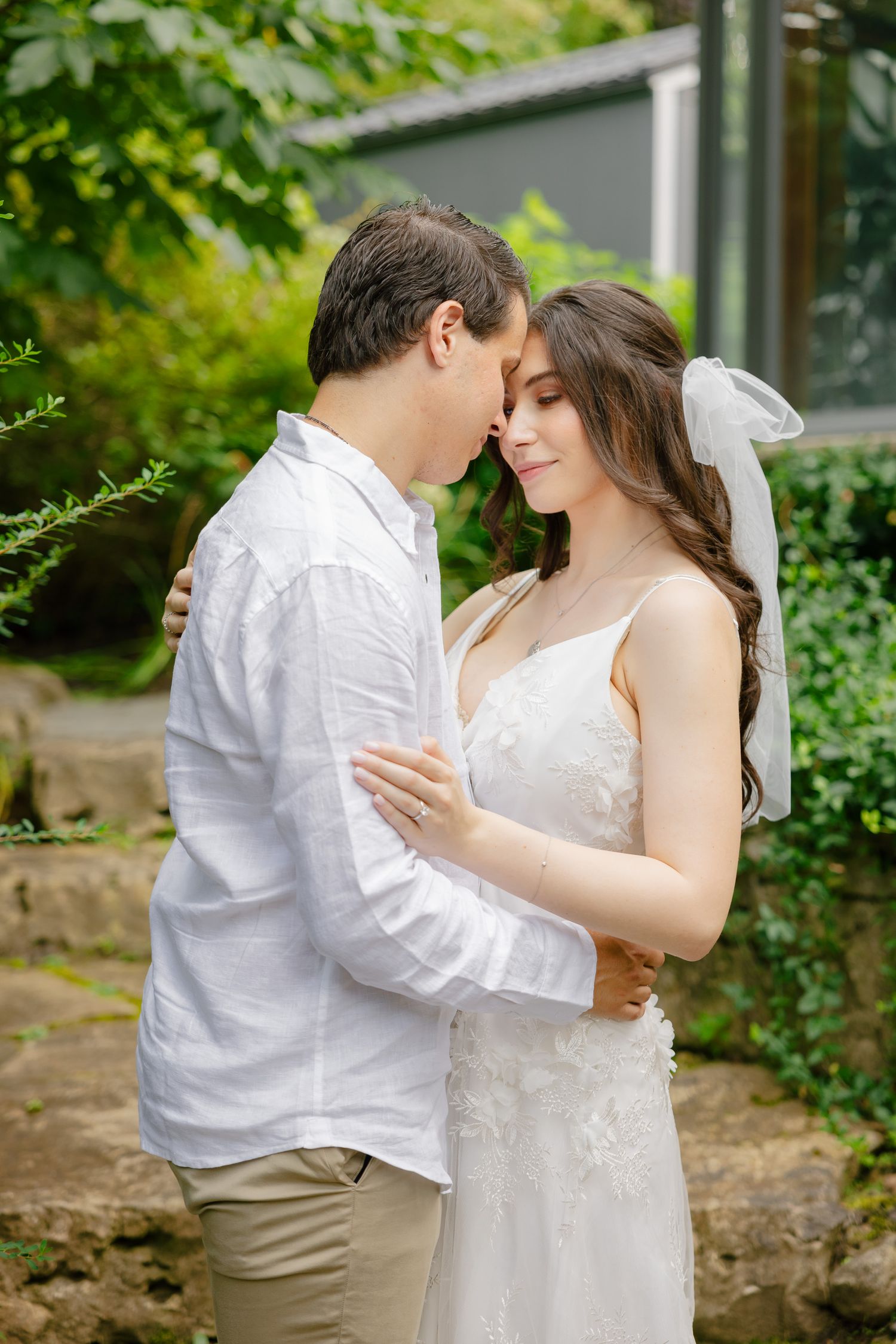 Intimate wedding portrait of couple embracing in front of a rustic greenhouse.