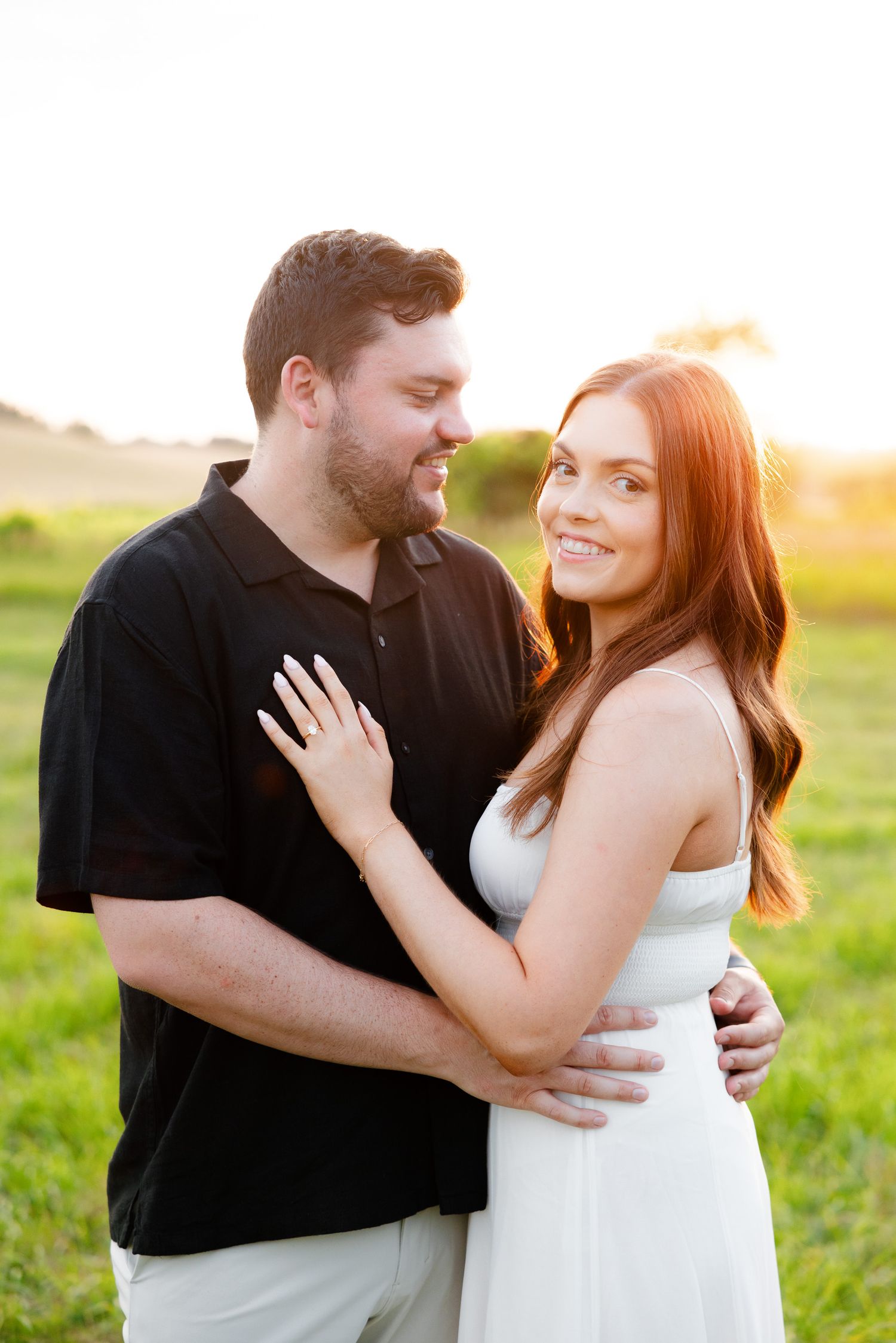 A couple shares an intimate moment during their sunset engagement session in a grassy field.