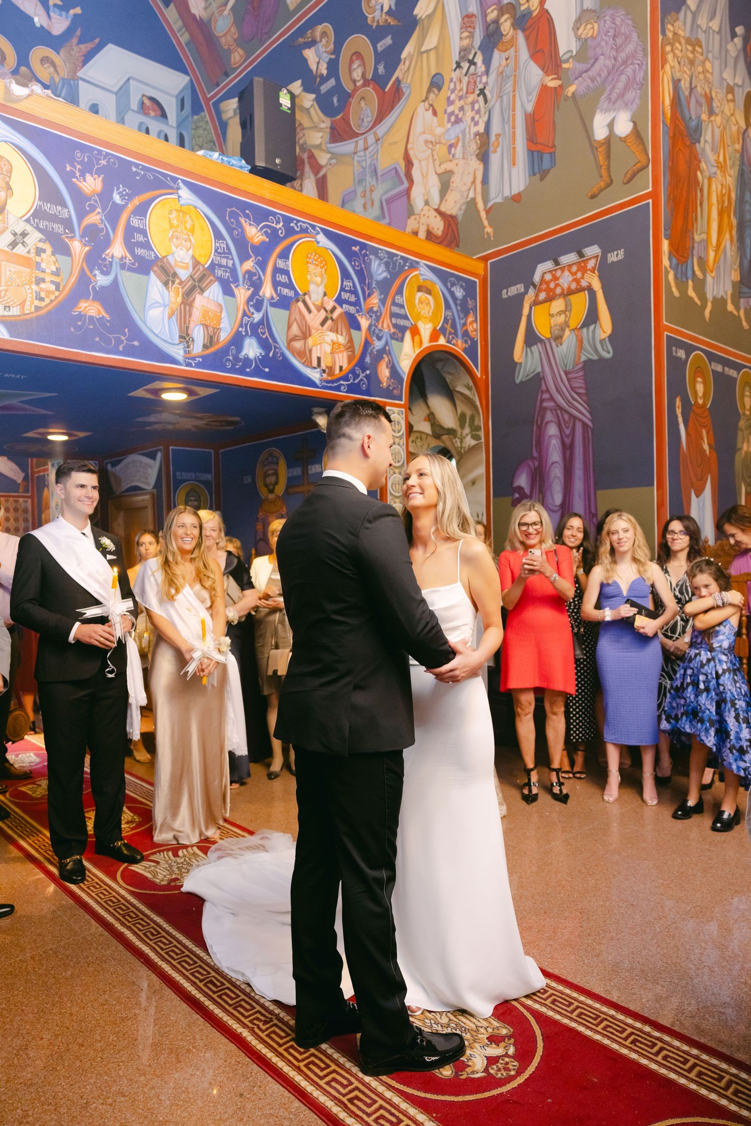 A wedding ceremony takes place in a beautiful church with ornate religious murals and frescoes adorning the walls.