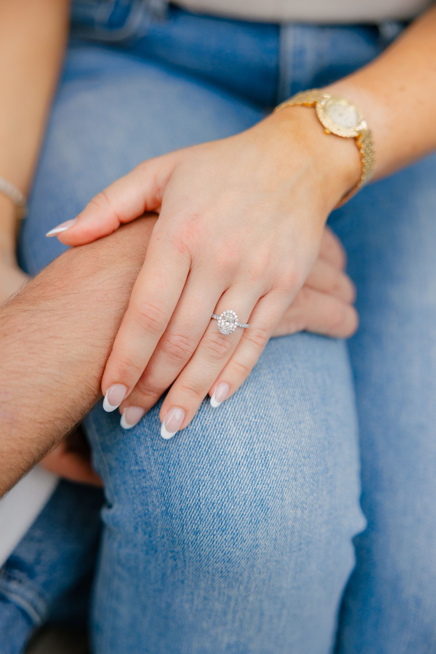 Close-up of hands showing engagement ring and gold watch against denim background.