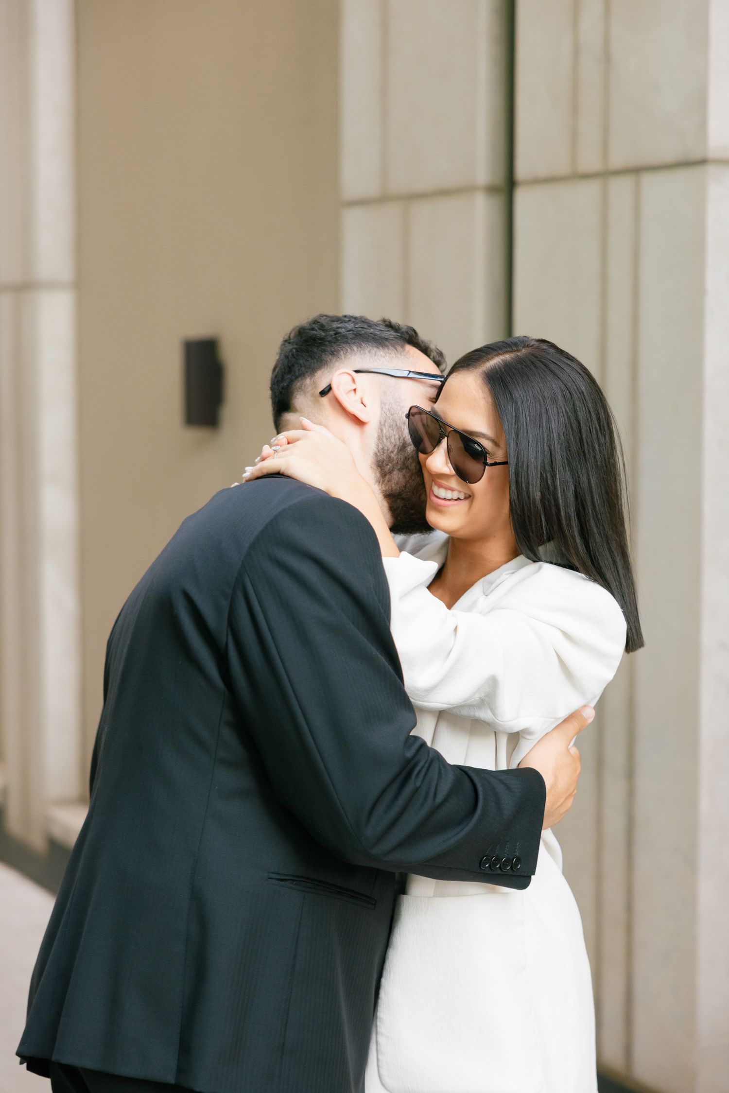 A stylish couple embraces outside a modern building in contrasting black and white outfits.