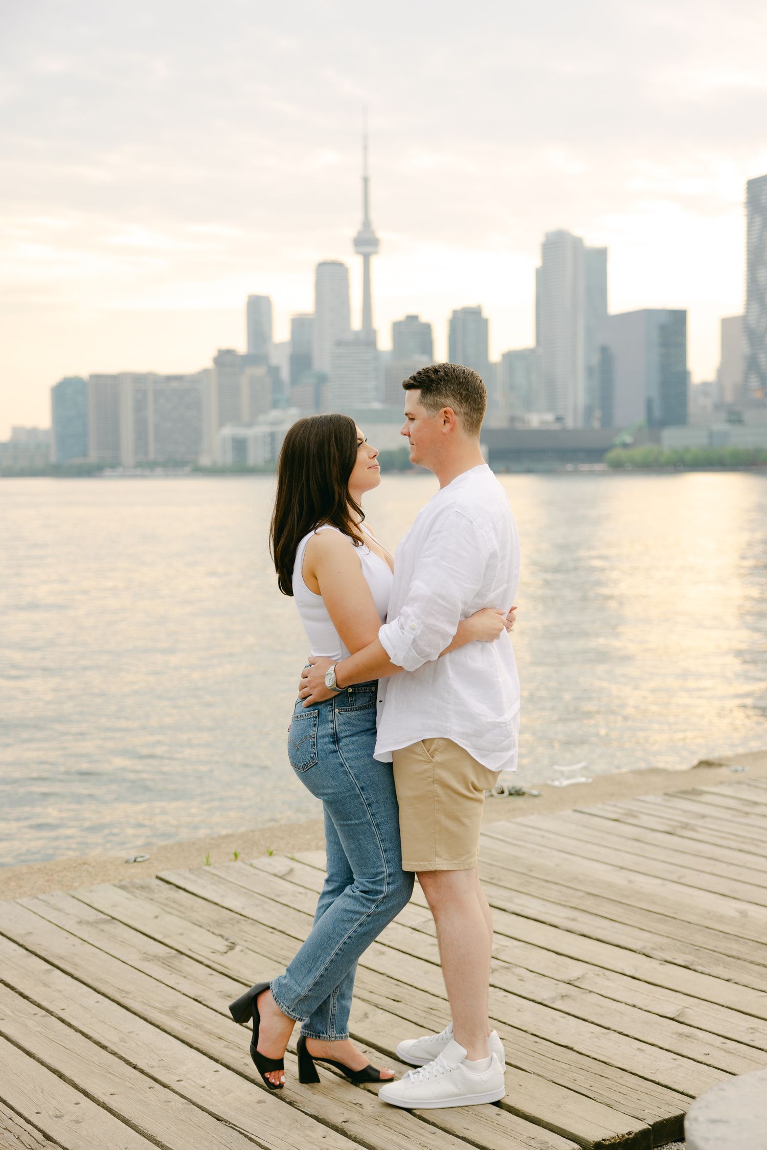Couple shares intimate moment on wooden pier with Toronto's iconic skyline behind them.