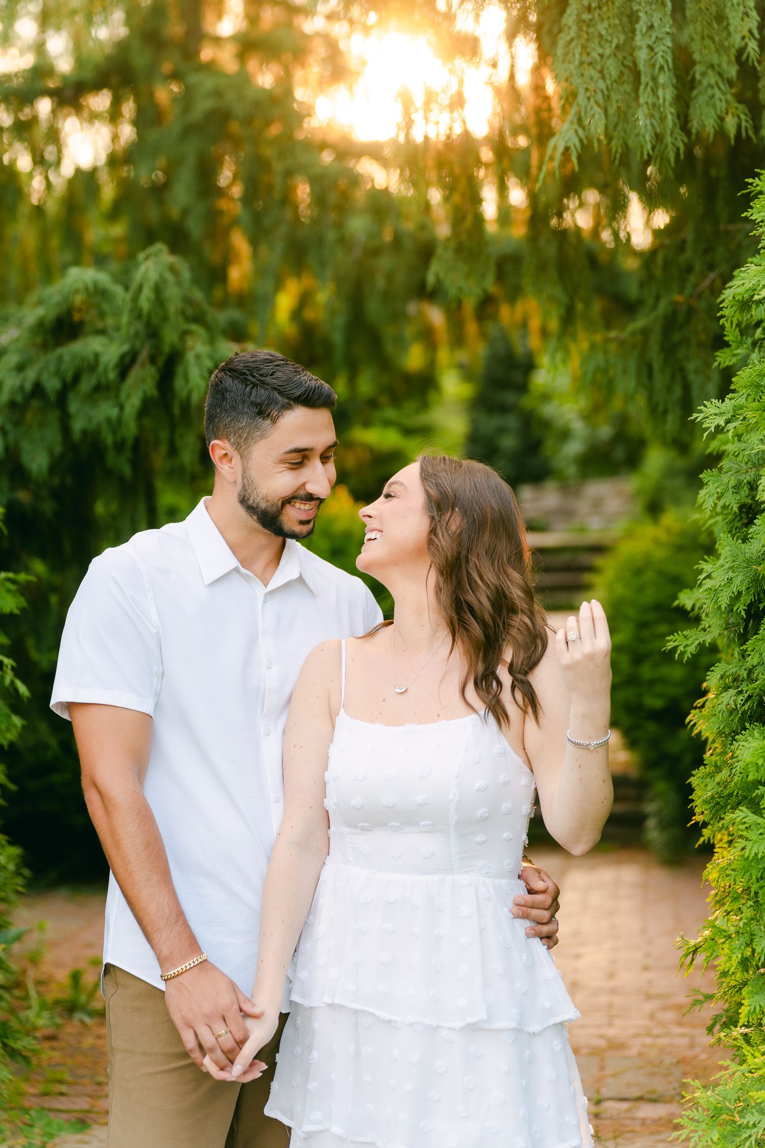Couple holds hands while sharing a loving look on a garden path at sunset.