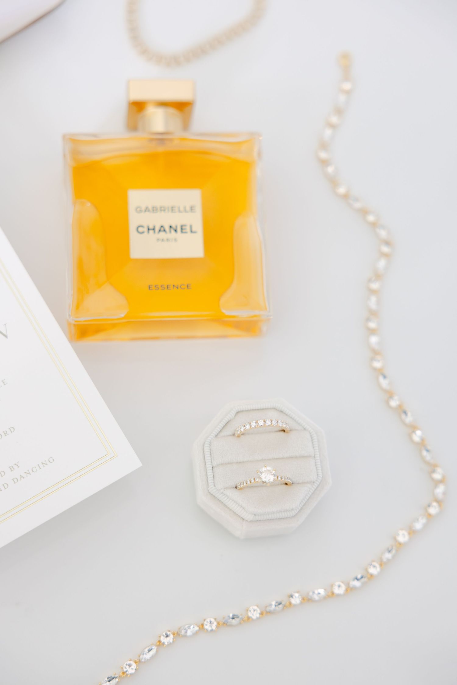 Orange Chanel perfume bottle with pearl necklace and ring box on white surface.