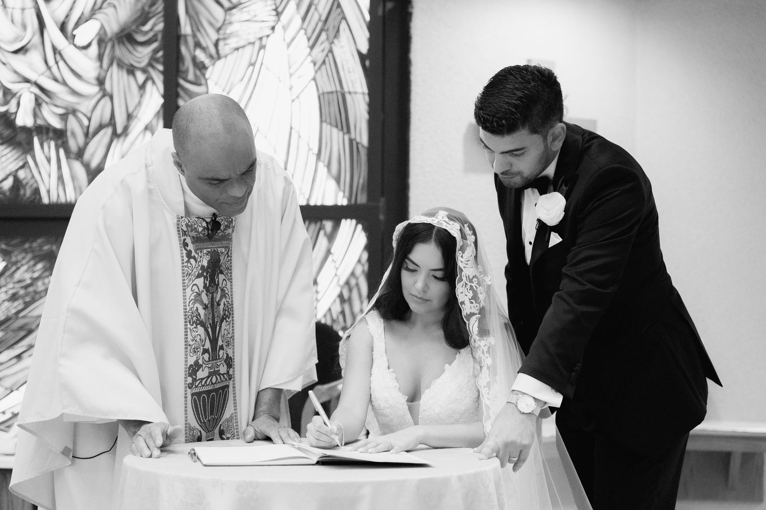 A marriage ceremony signing moment in black and white with priest and couple at the altar.