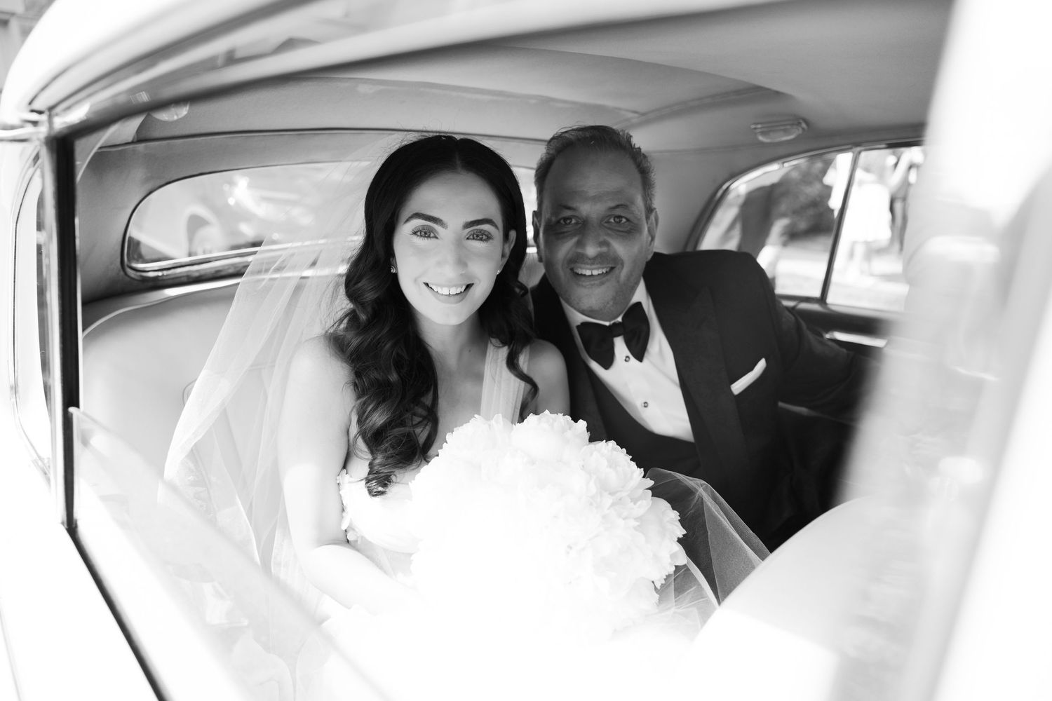 Interior shot of bride and companion in vintage car on wedding day.