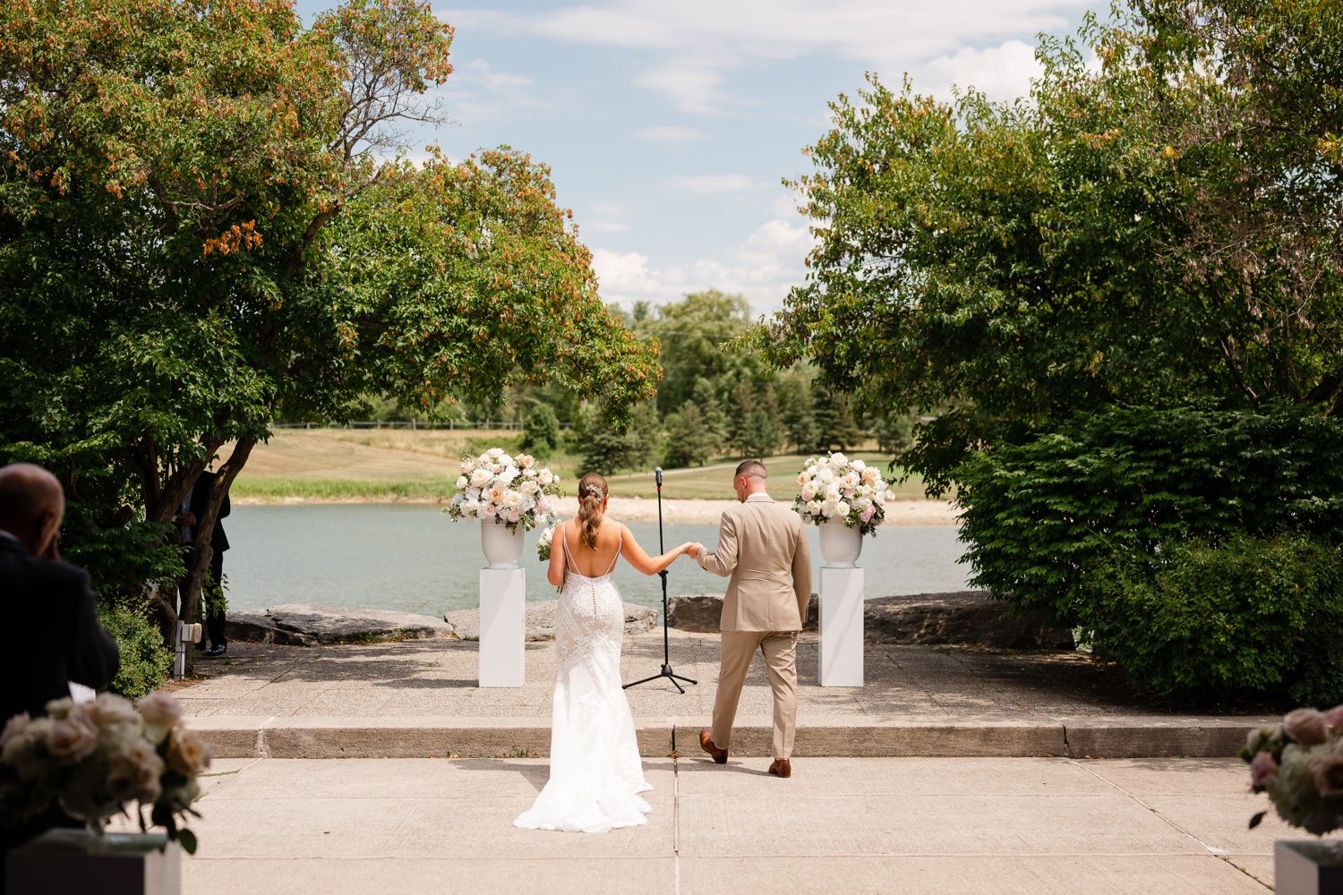 Elegant outdoor wedding ceremony setup overlooking a serene pond with white floral pedestals.