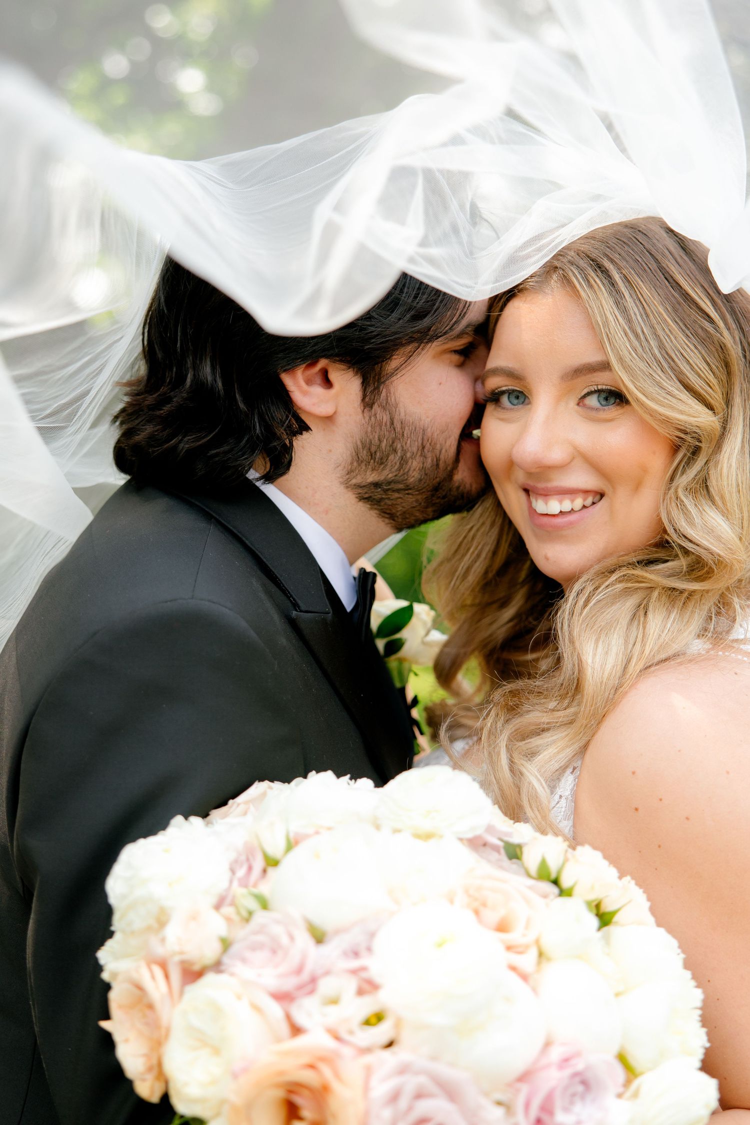 A tender garden wedding moment with flowing veil and pastel rose bouquet.