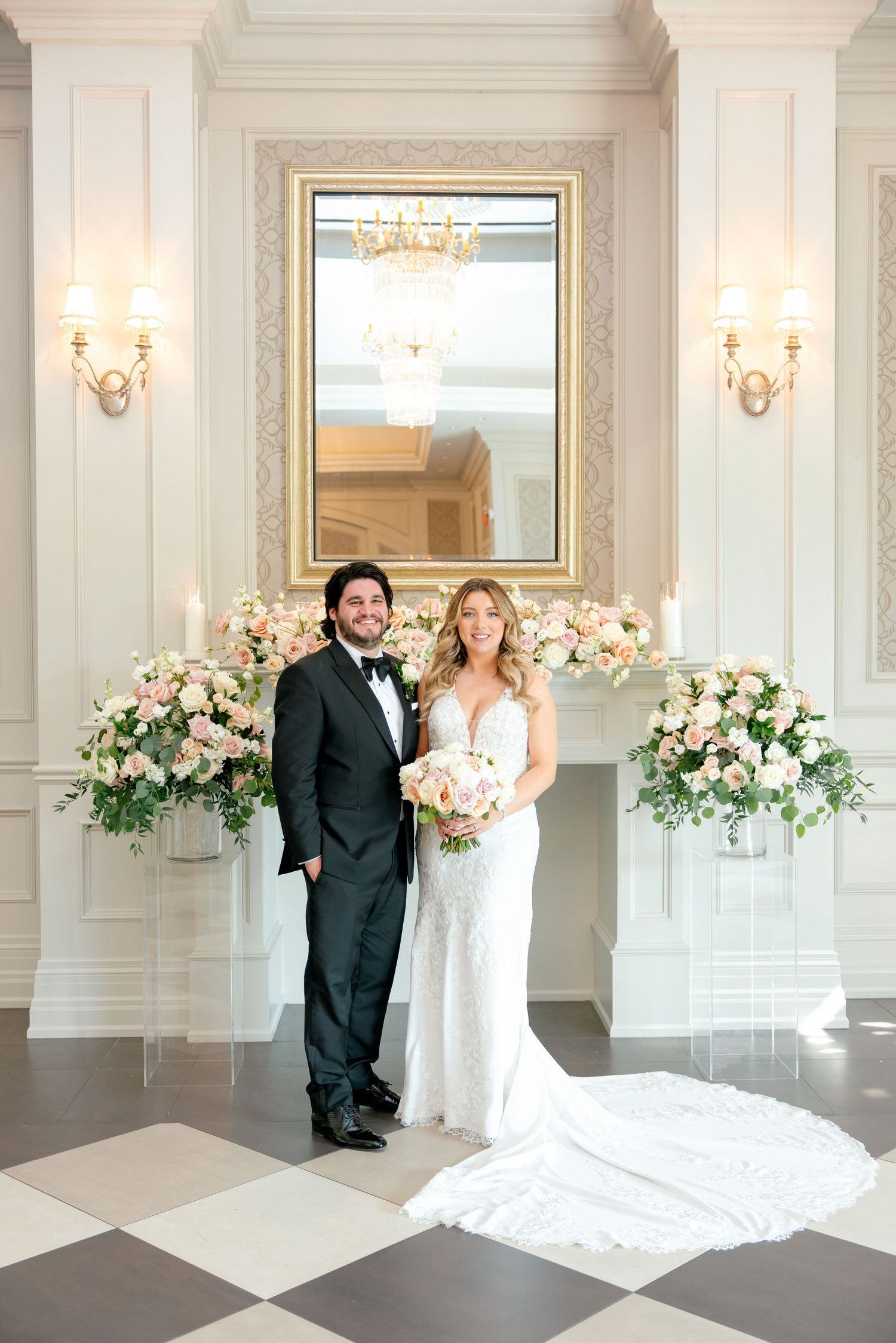 Elegant wedding portrait setup with ornate mirror, wall sconces and floral arrangements.
