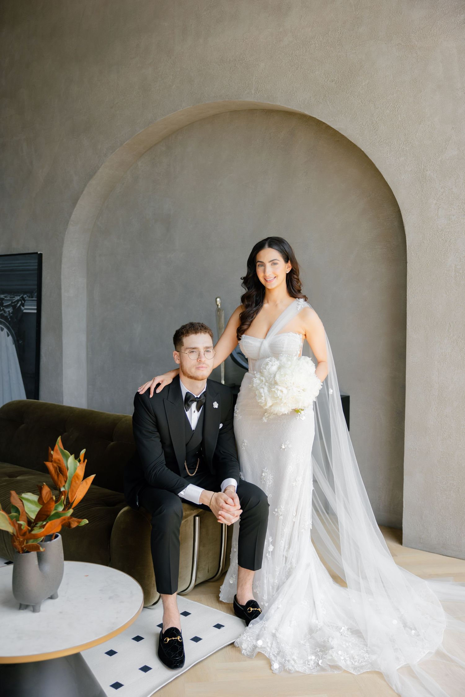 Wedding couple poses together in elegant attire under an arched doorway with modern decor.