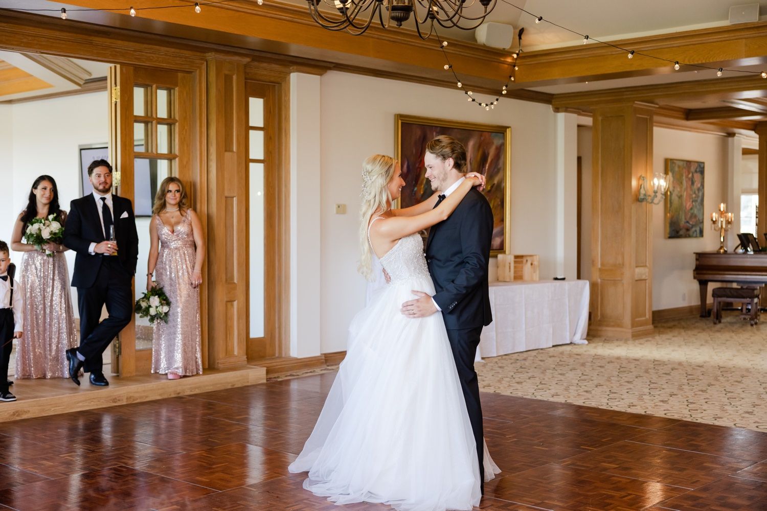 Wedding dance in progress with guests watching in an elegant wood-trimmed ballroom.