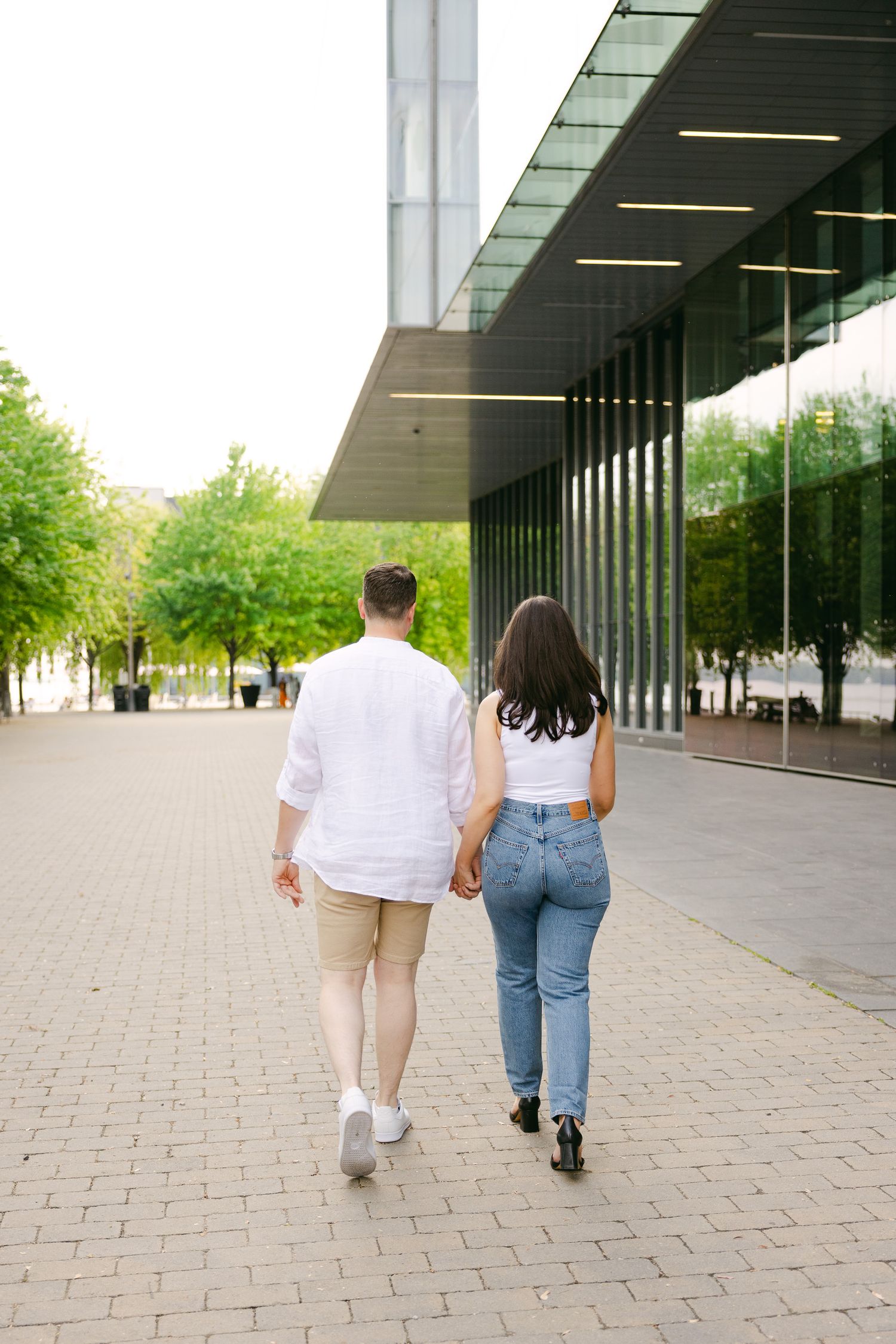 A couple walking together along a modern building with glass walls and brick pavement.
