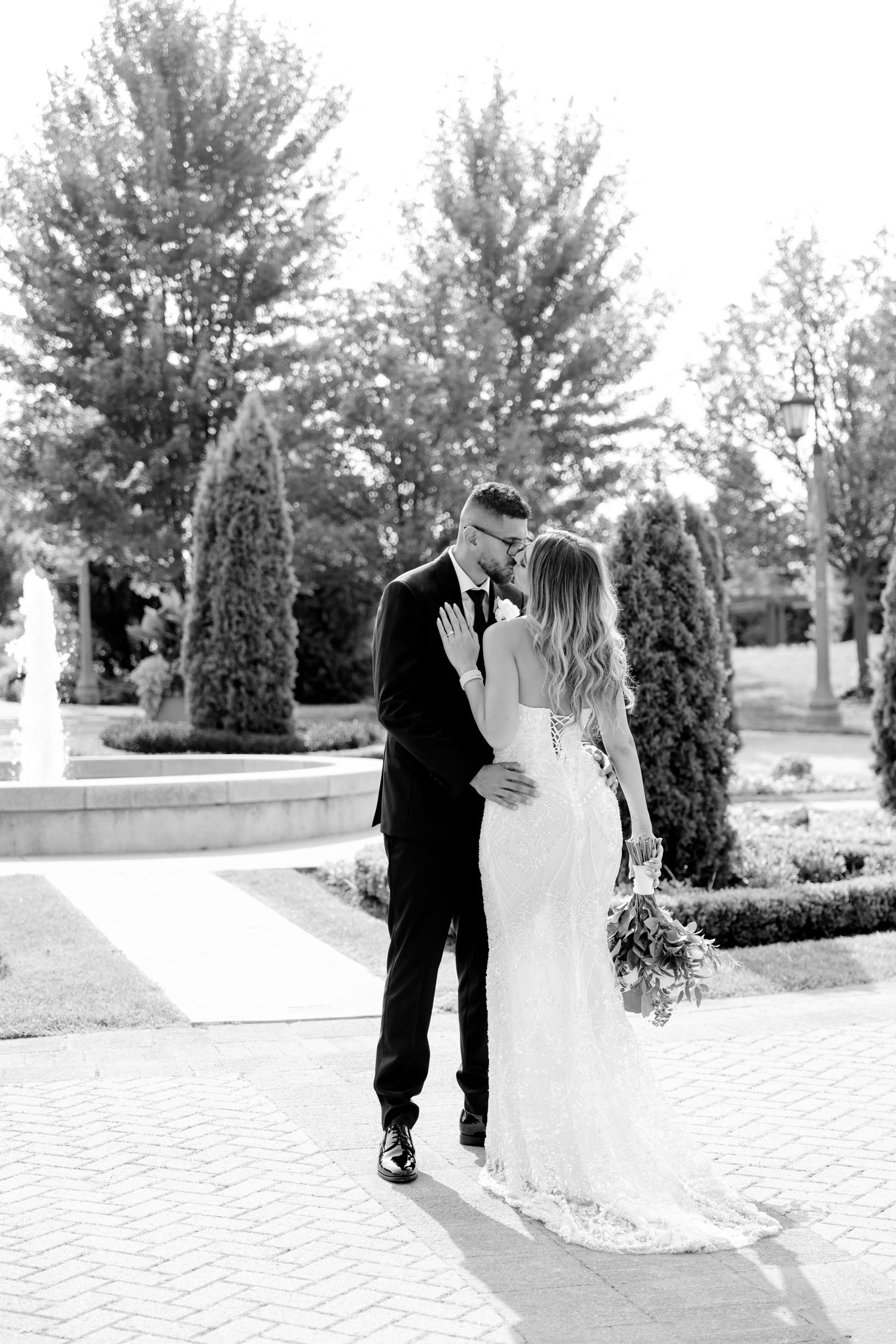 Black and white portrait of newlyweds embracing in a formal garden setting with decorative pathways.