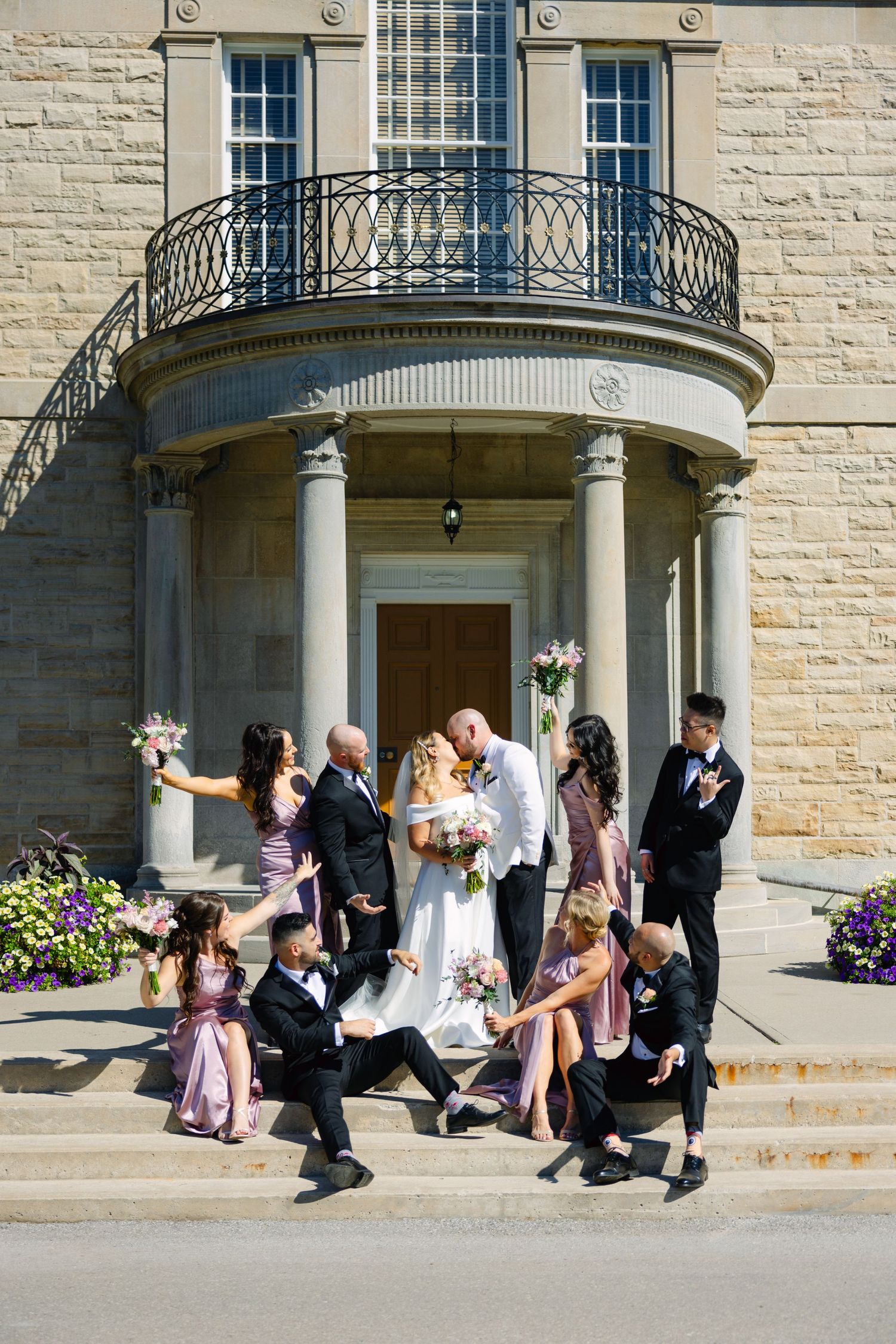 Energetic wedding party photo with attendants dancing on stone steps of historic venue.