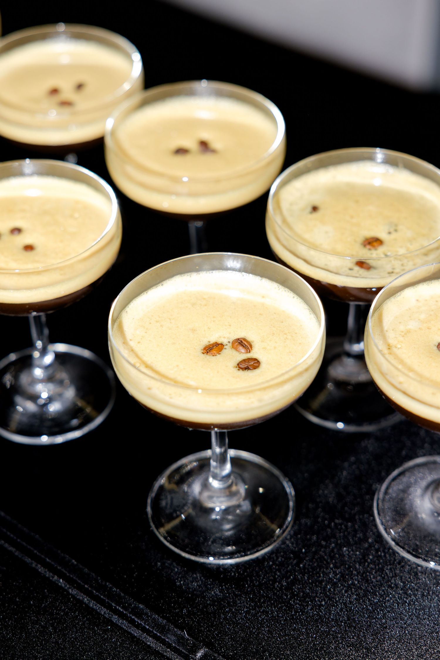 Creamy cocktails garnished with coffee beans served in coupe glasses on a dark surface.