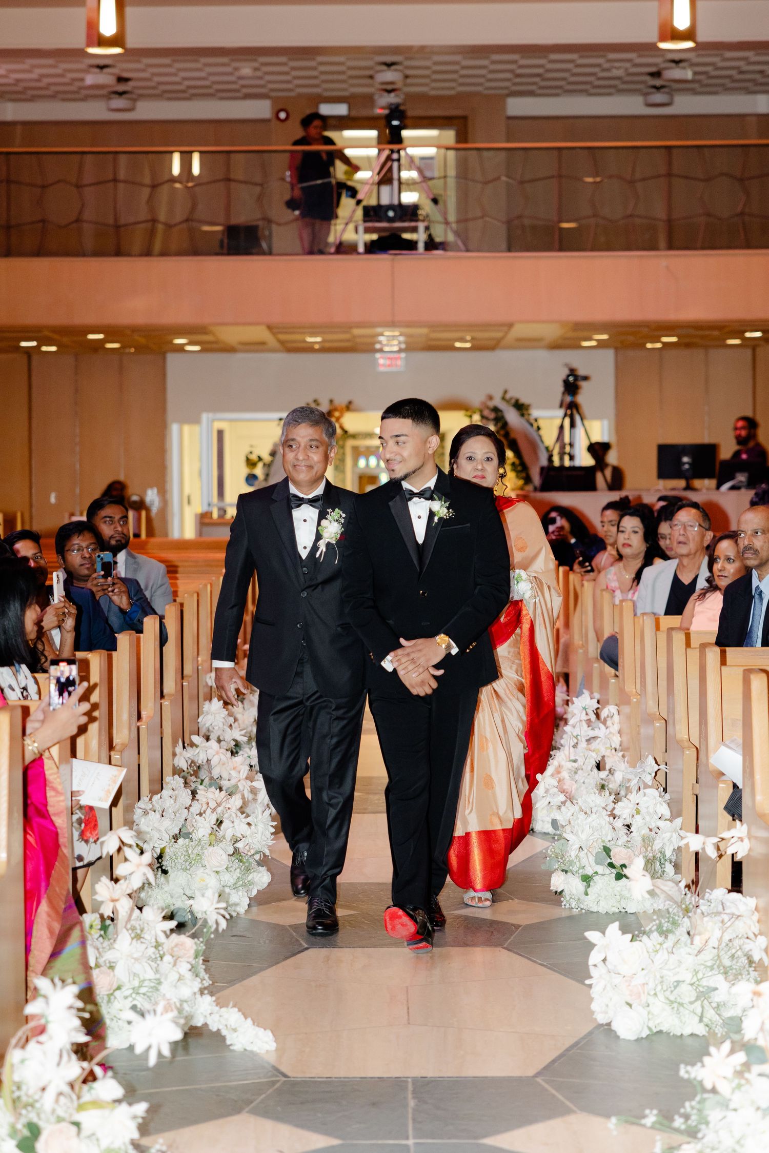 Wedding ceremony processional in modern church with white floral aisle decorations.