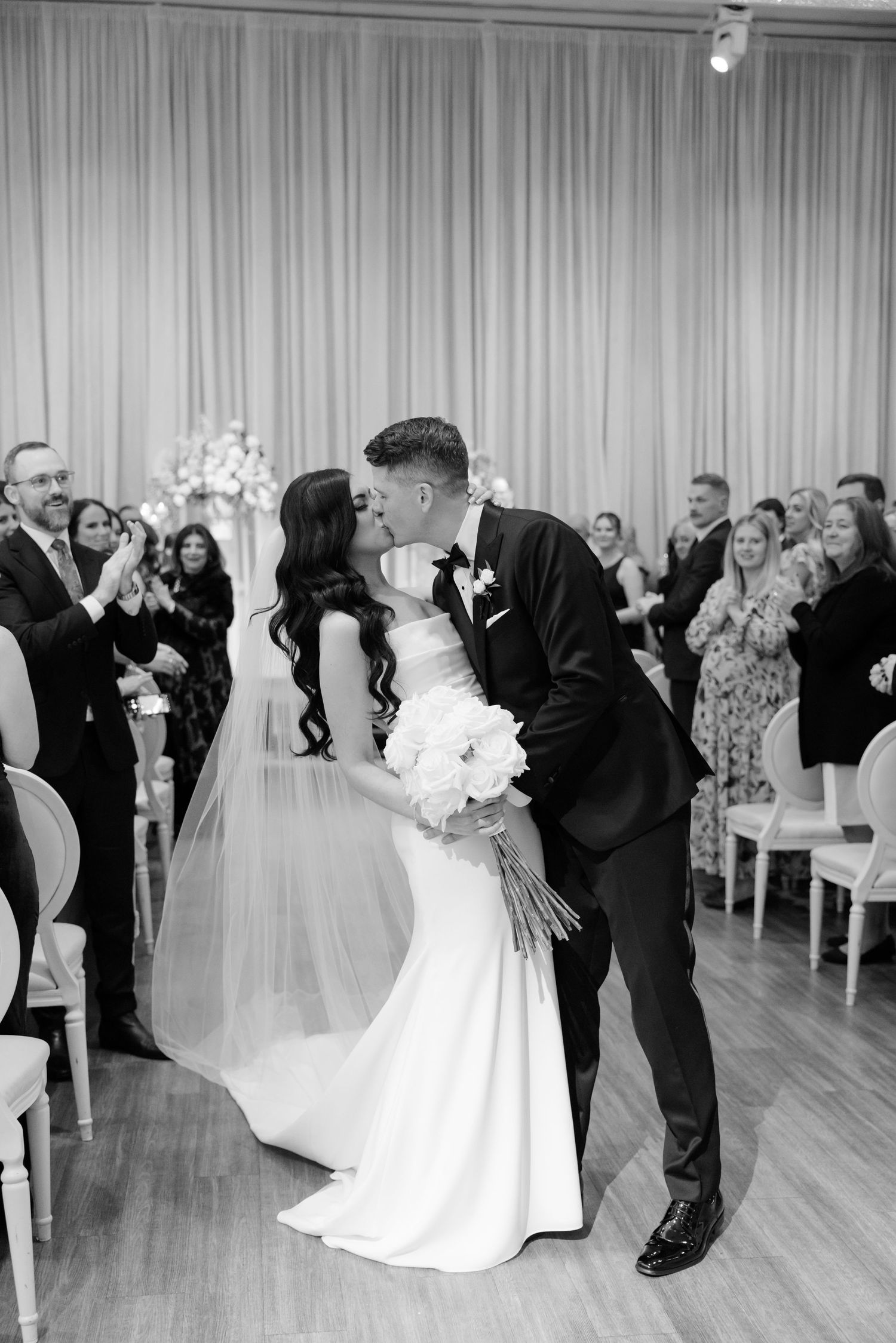 A black and white capture of newlyweds sharing their first kiss at the ceremony.