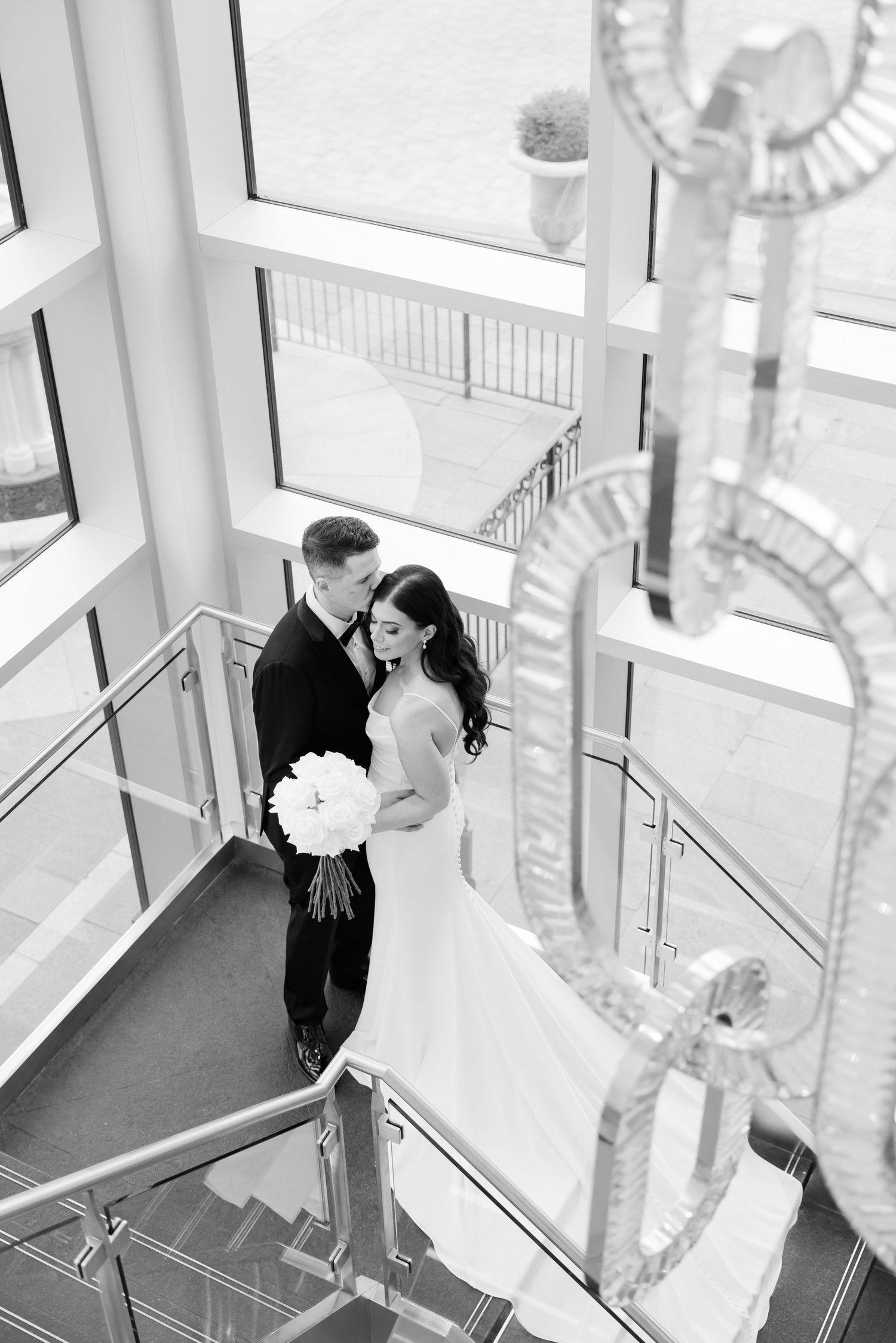 Elegant black and white wedding photo on modern staircase with dramatic lighting.