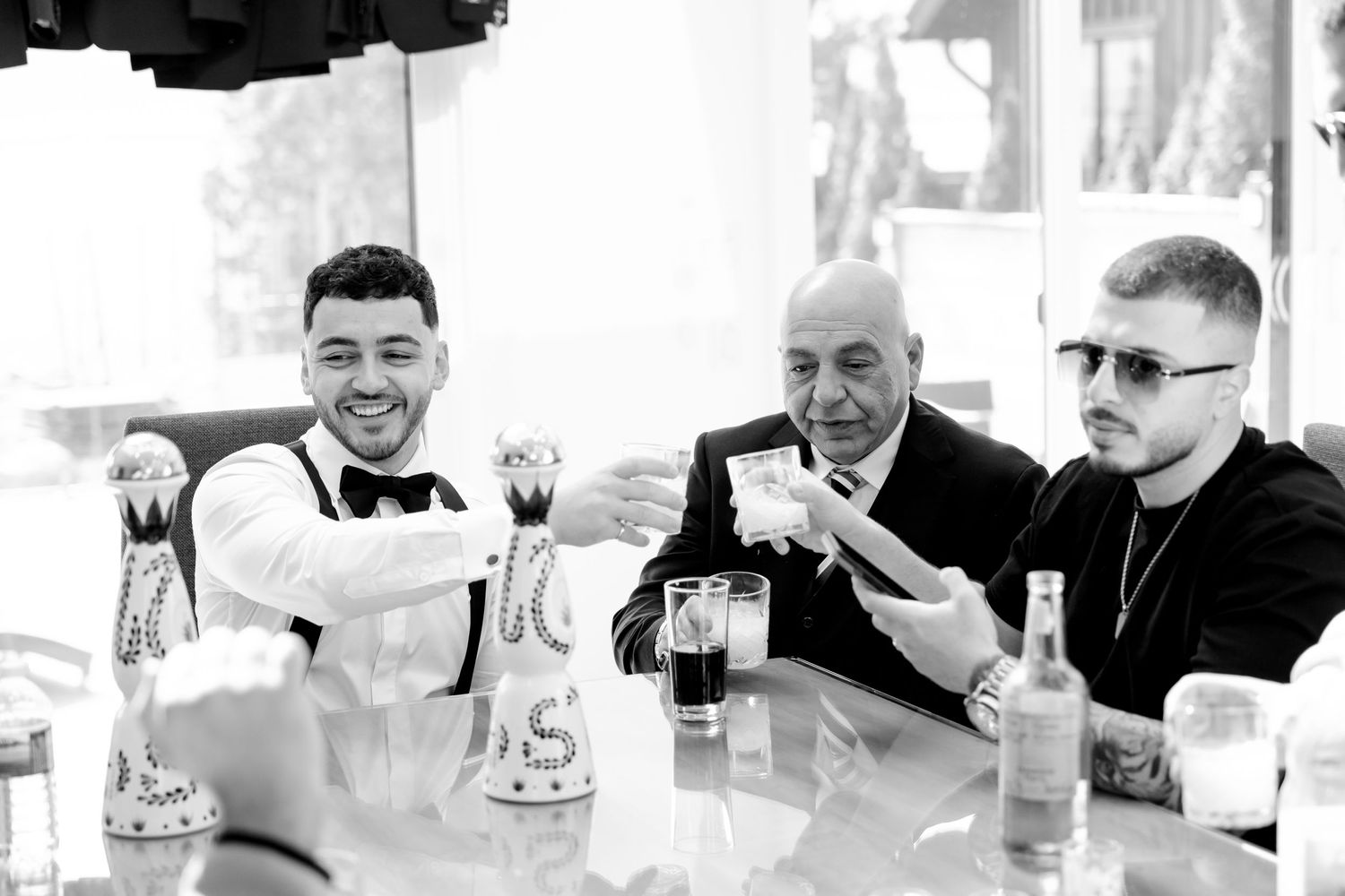 Three people sit at a table sharing drinks and laughs during a celebratory gathering.