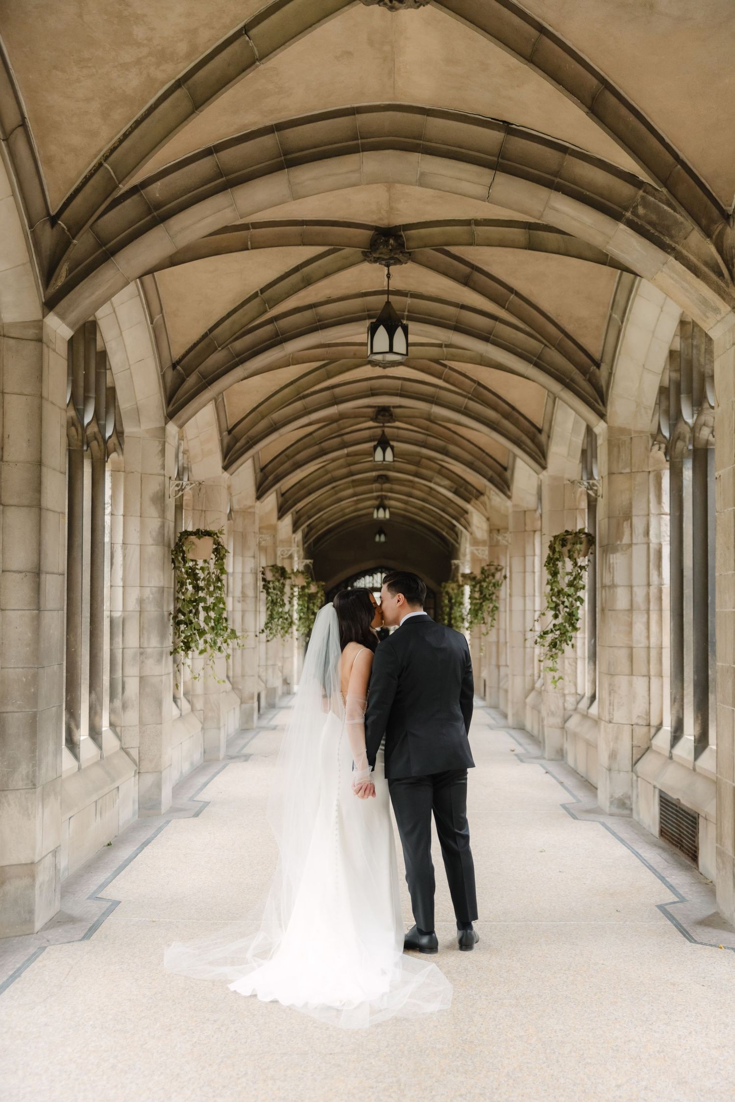 Newlyweds share romantic moment under vaulted stone ceiling with decorative greenery.