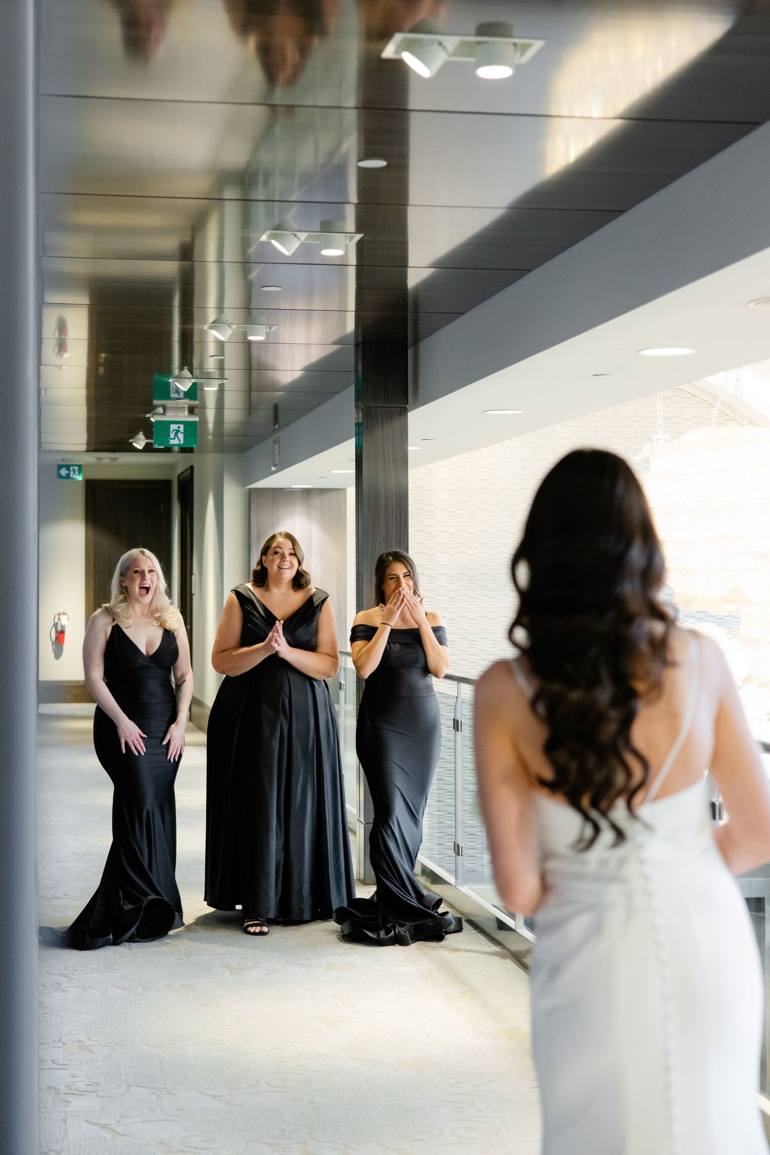 Bridesmaids in black dresses react with joy during a first look reveal with the bride.