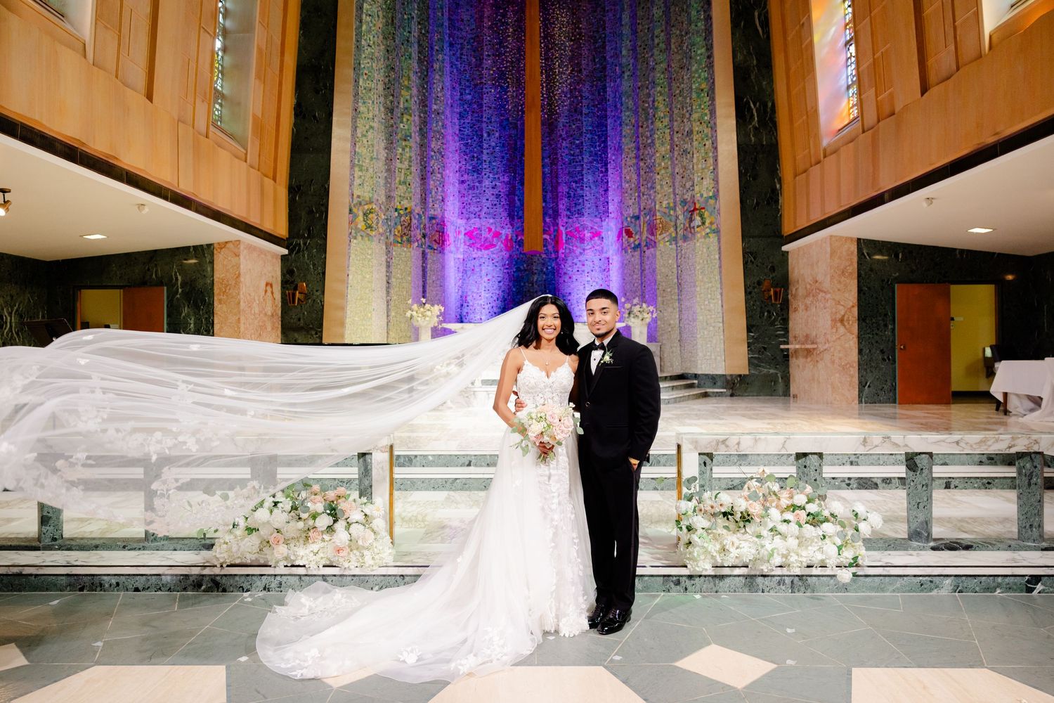 Elegant church wedding photo with dramatic veil and purple cross illumination.