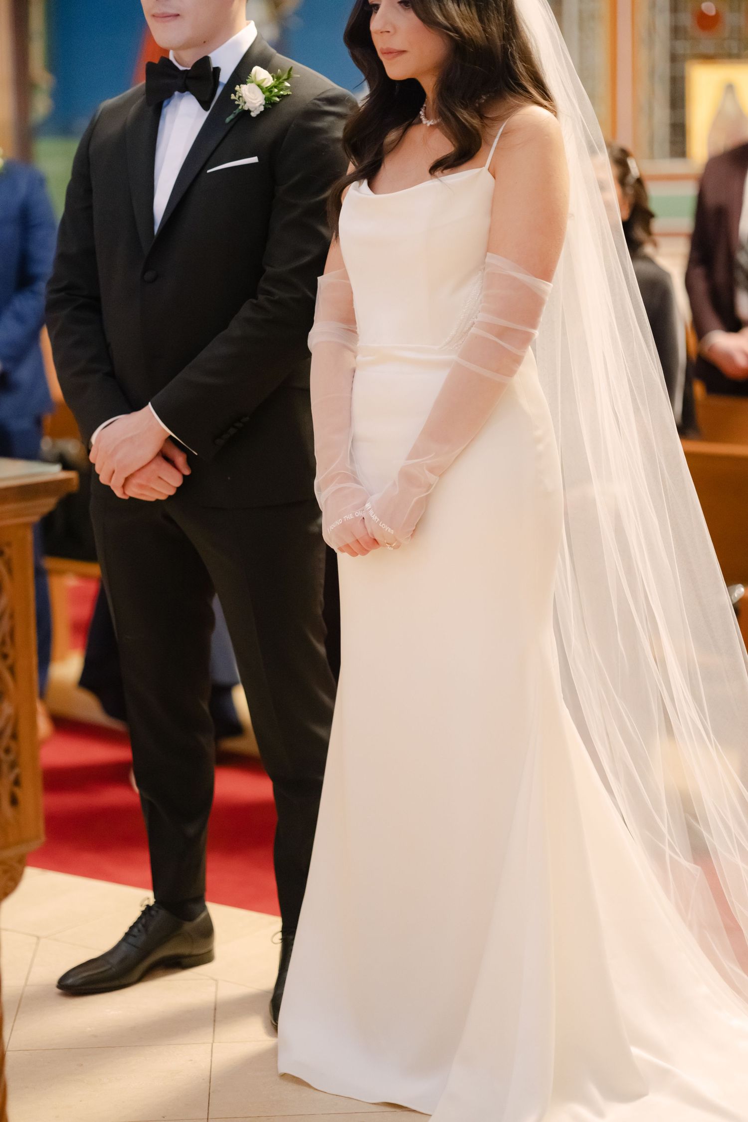 Side view of couple during wedding ceremony showing bride's flowing veil and groom's classic tuxedo.