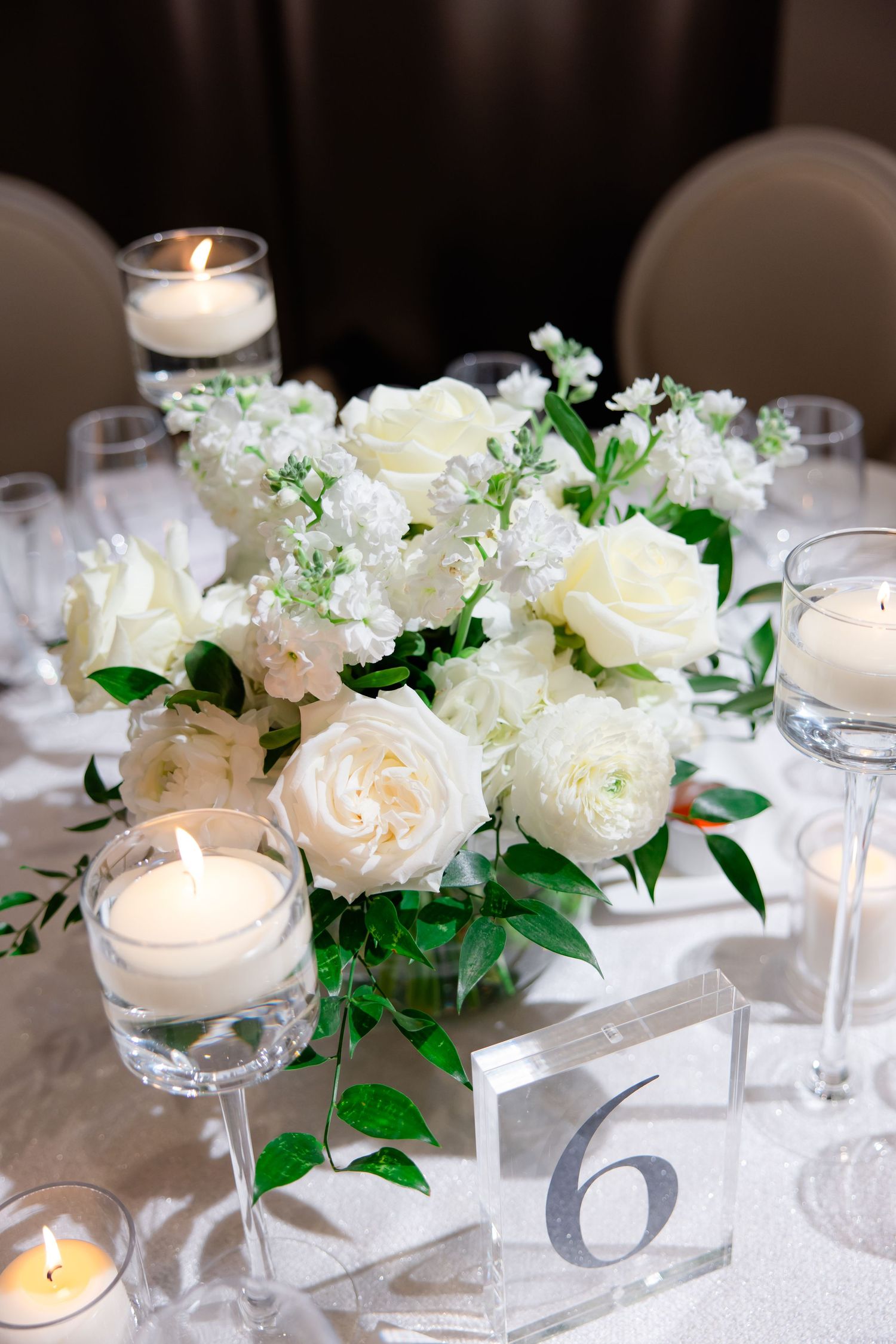 White roses and candlelight centerpiece with table number six marker on formal dining table.