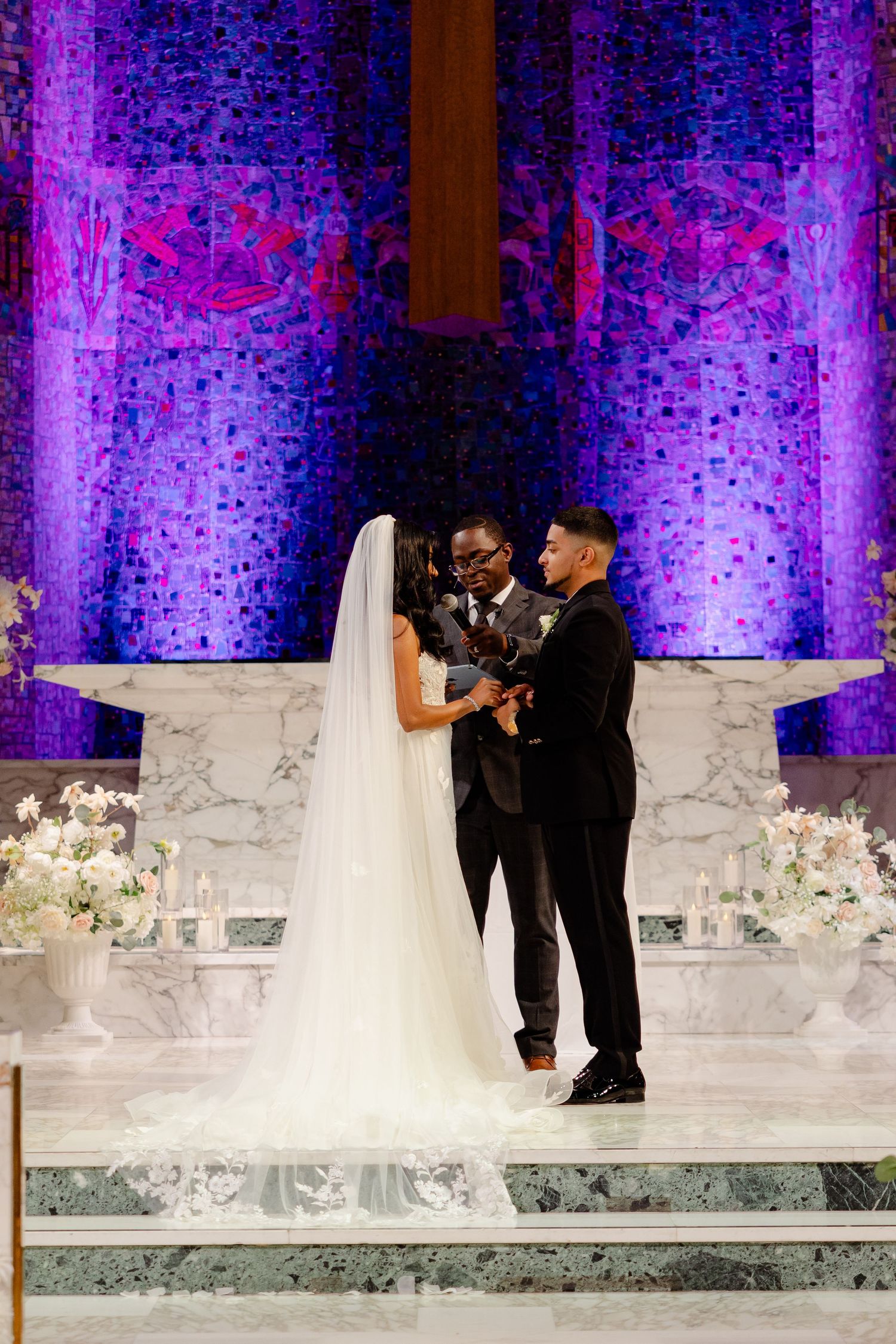 Intimate wedding ceremony moment at church altar with dramatic purple lighting and floral decor.