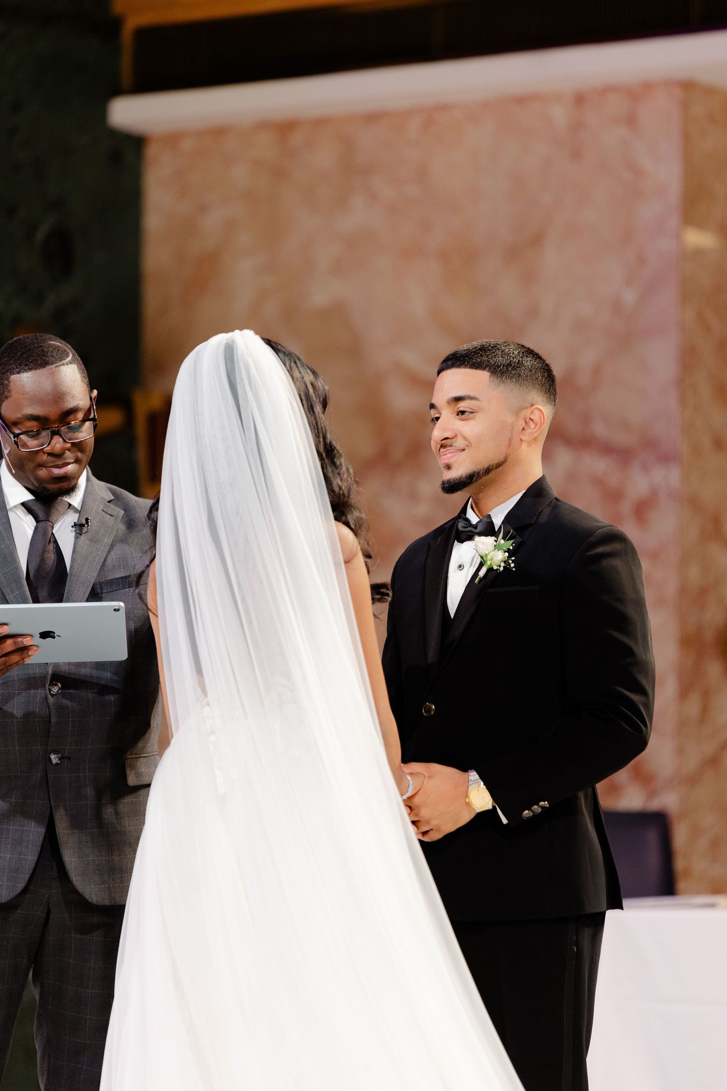 Wedding ceremony in progress with officiant reading from tablet as couple exchanges vows.