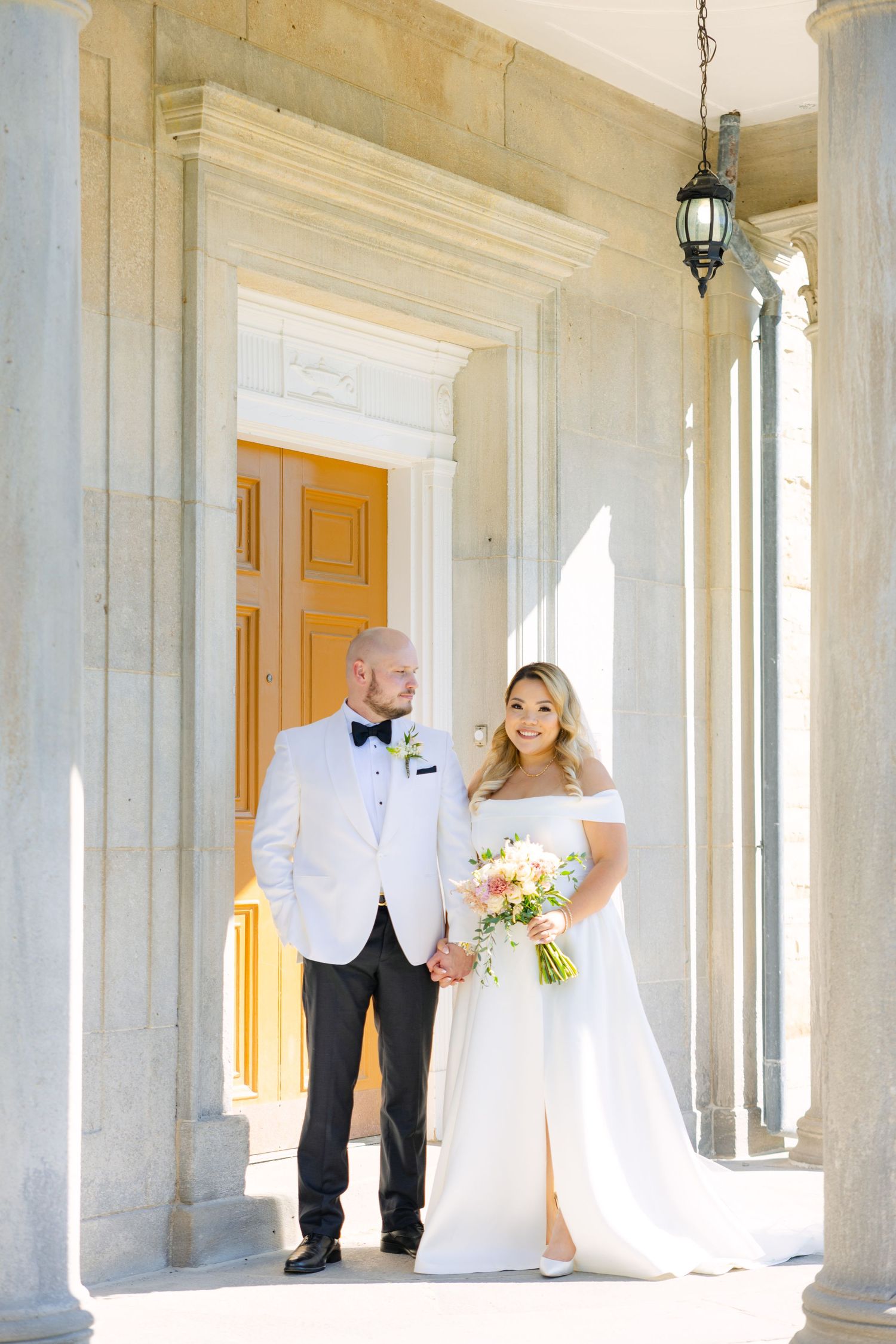 An elegant wedding portrait framed by white columns and a wooden door entrance.