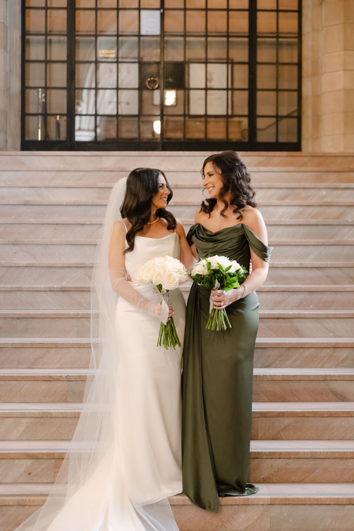 Two people in formal wear share a joyful moment on elegant stone steps with vaulted ceiling above.