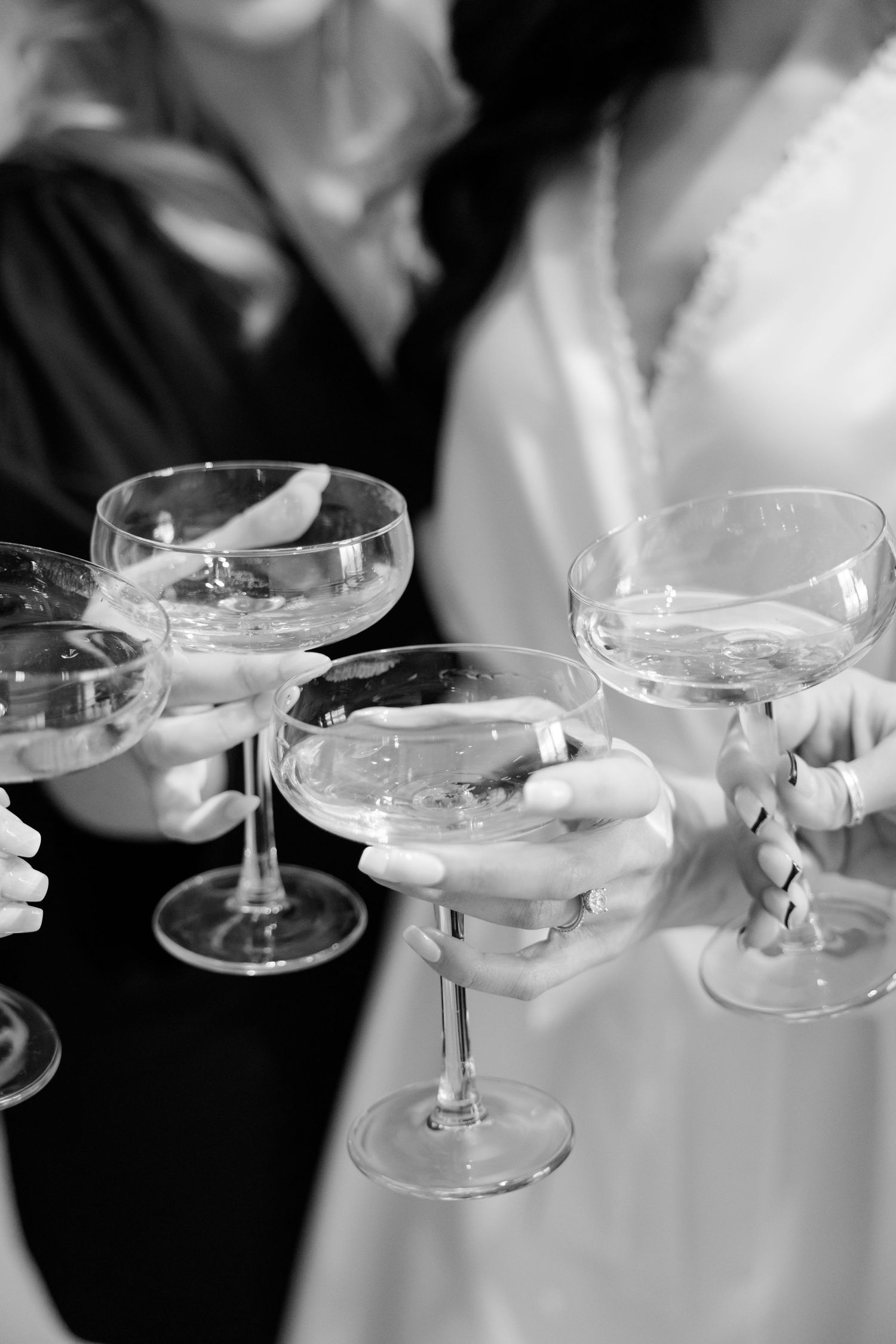 Hands holding champagne coupes in a celebratory toast, black and white photography.