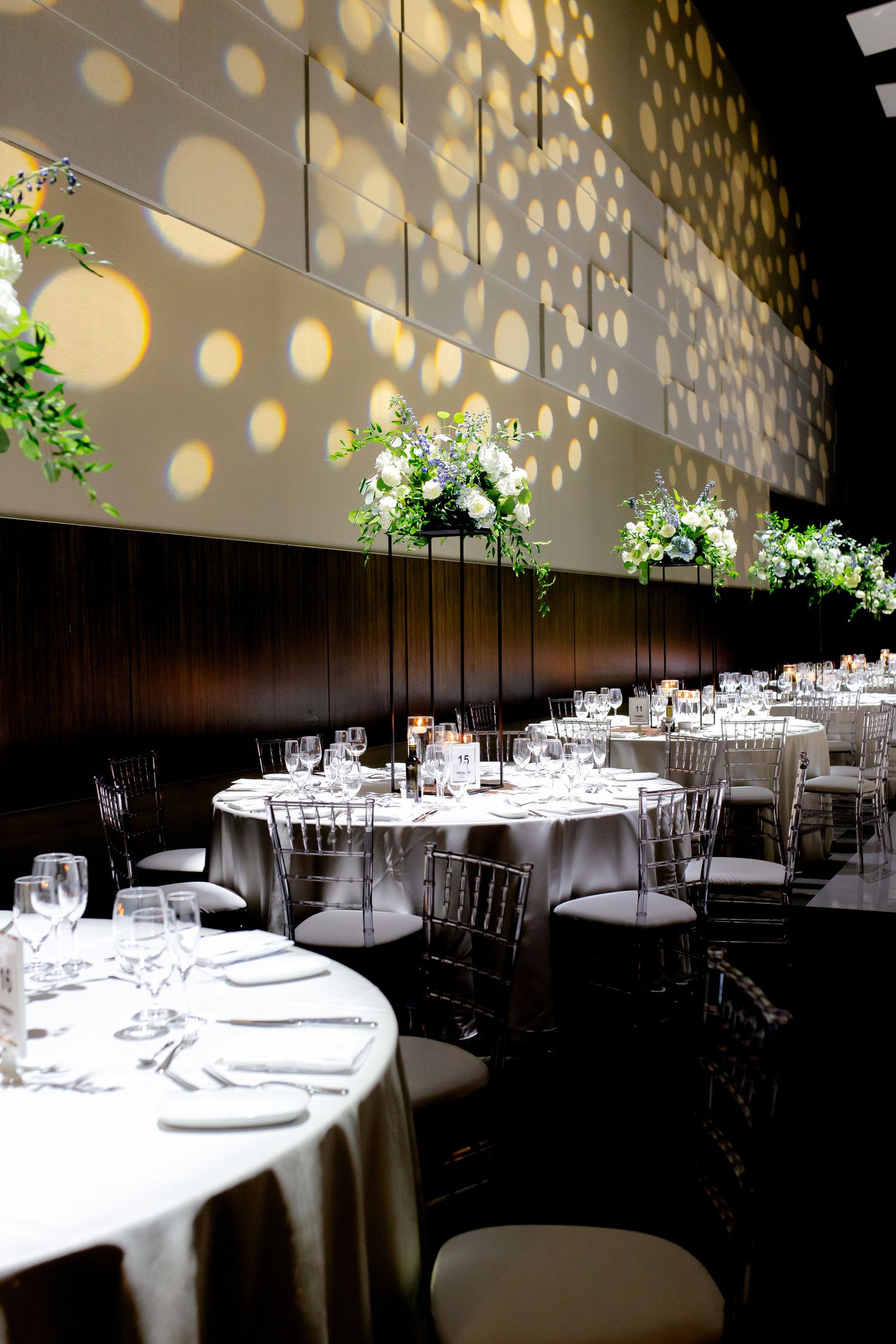 Elegant wedding reception setup with round tables and dramatic lighting creating circular patterns on the walls.