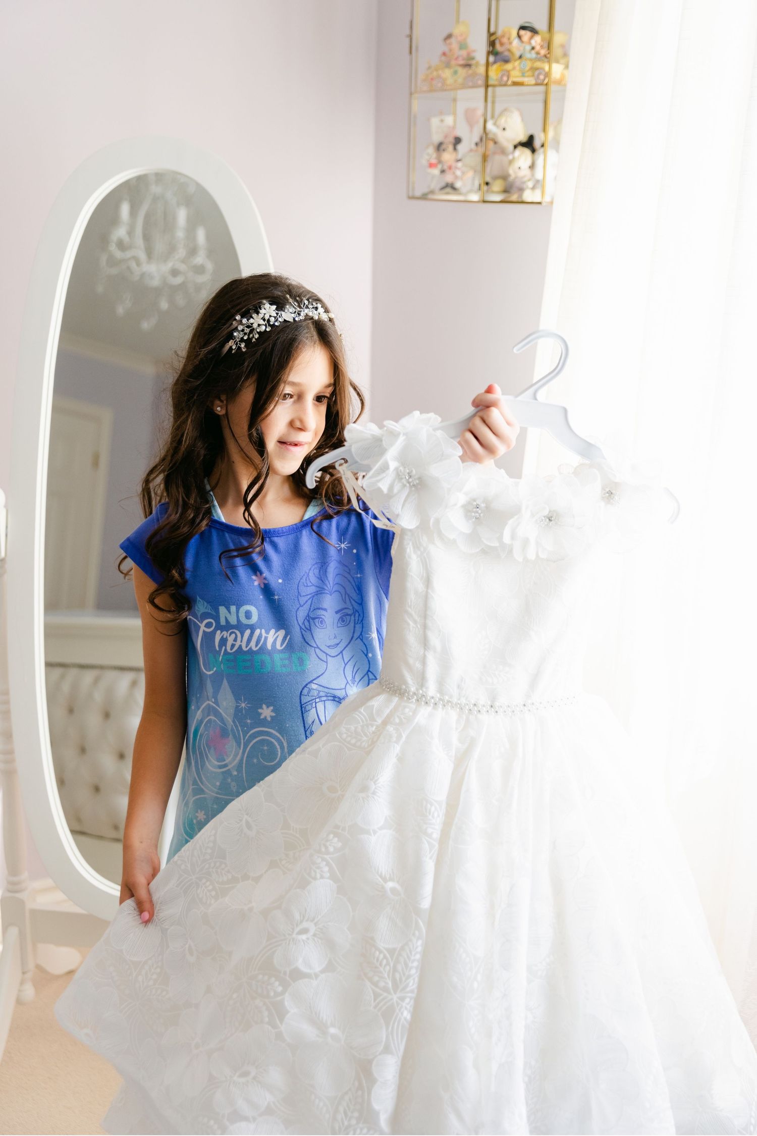 White lace wedding dress displayed next to mirror in elegant dressing room.