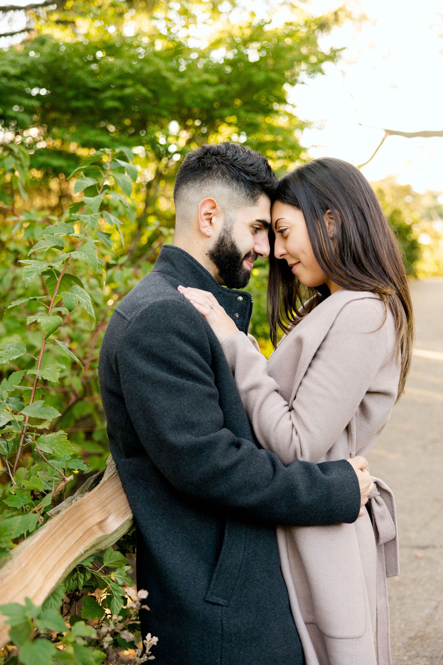 Romantic couple in coats sharing an intimate moment outdoors with autumn foliage in background.