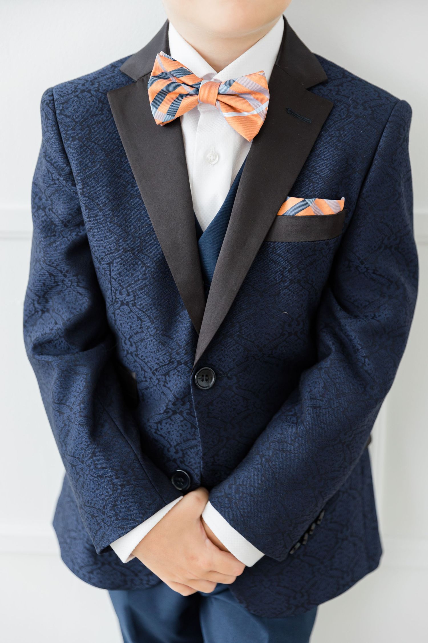 Close up of navy textured suit jacket with orange striped bowtie and pocket square.